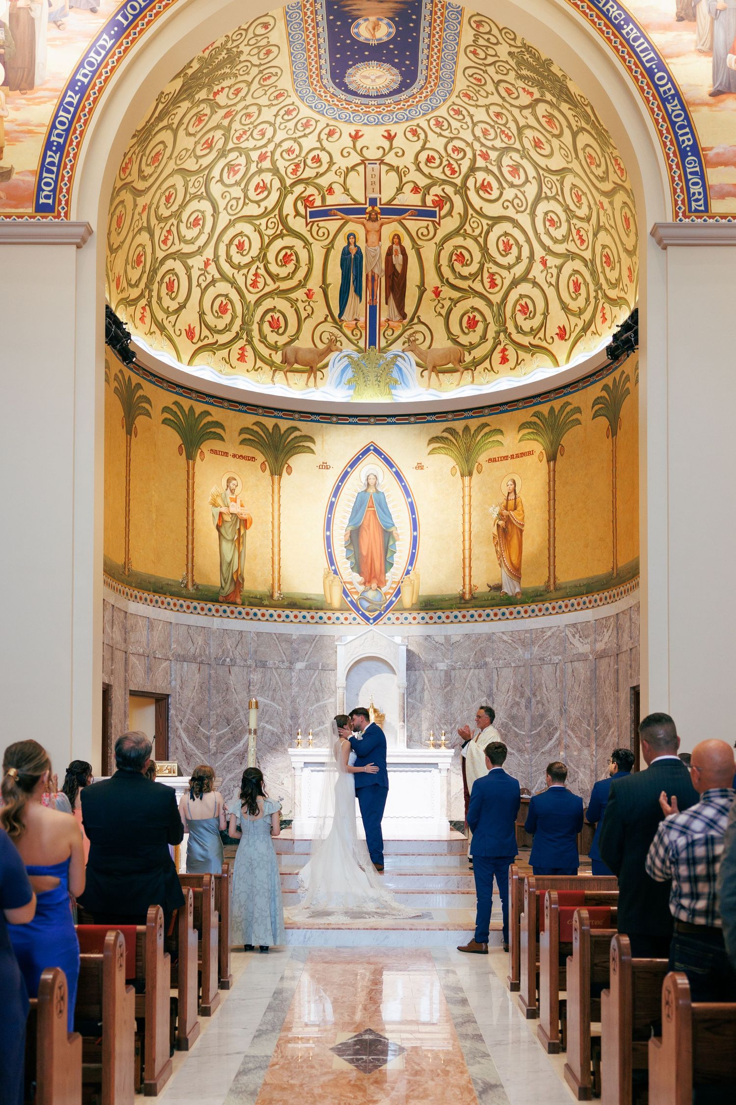 Elegant church interior with golden dome ceiling and religious artwork during a wedding ceremony.