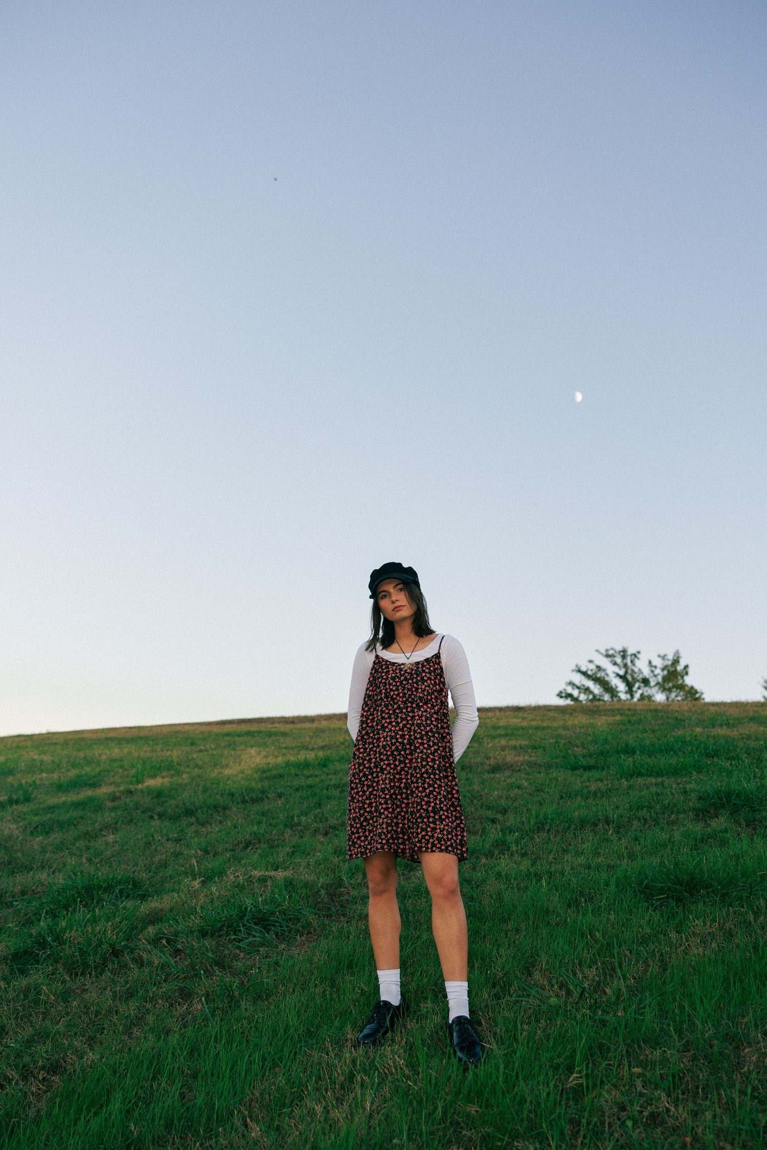 A figure in a polka dot dress poses against a rolling hill landscape at dusk.