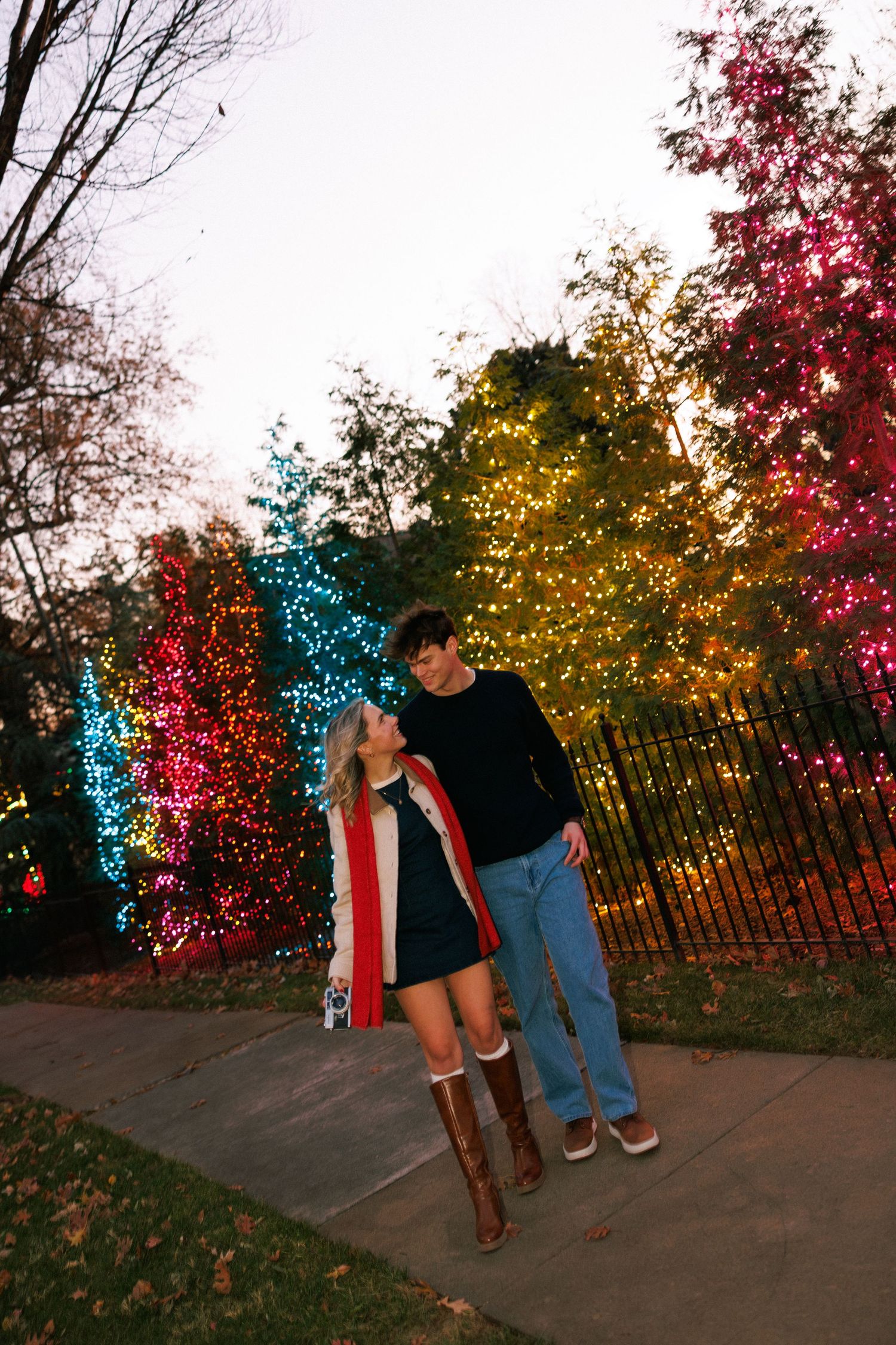 Couple standing in front of colorful illuminated trees with red and blue lights.