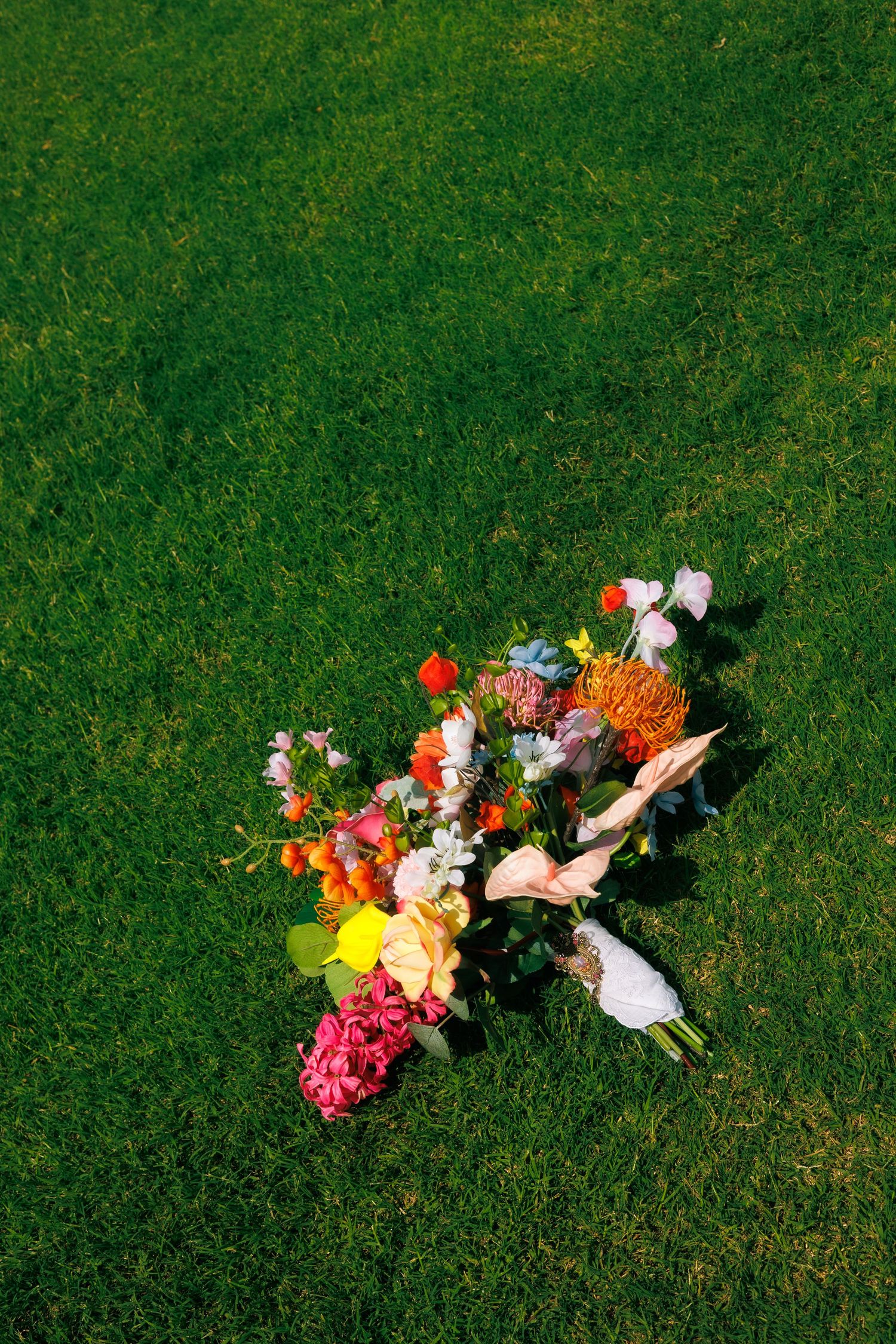 A colorful floral arrangement lies scattered on bright green grass.