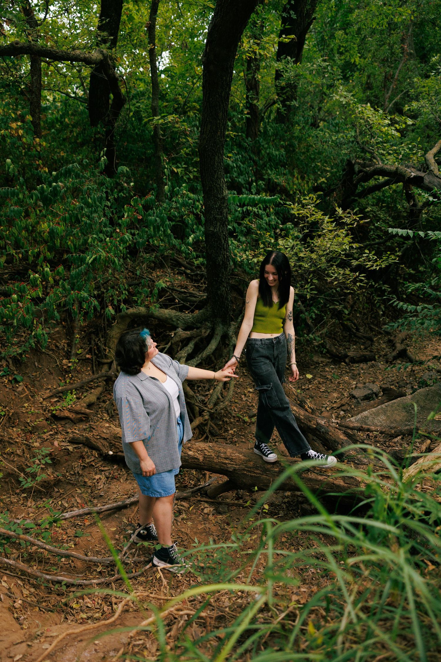 Two people helping each other navigate a wooded hiking trail.