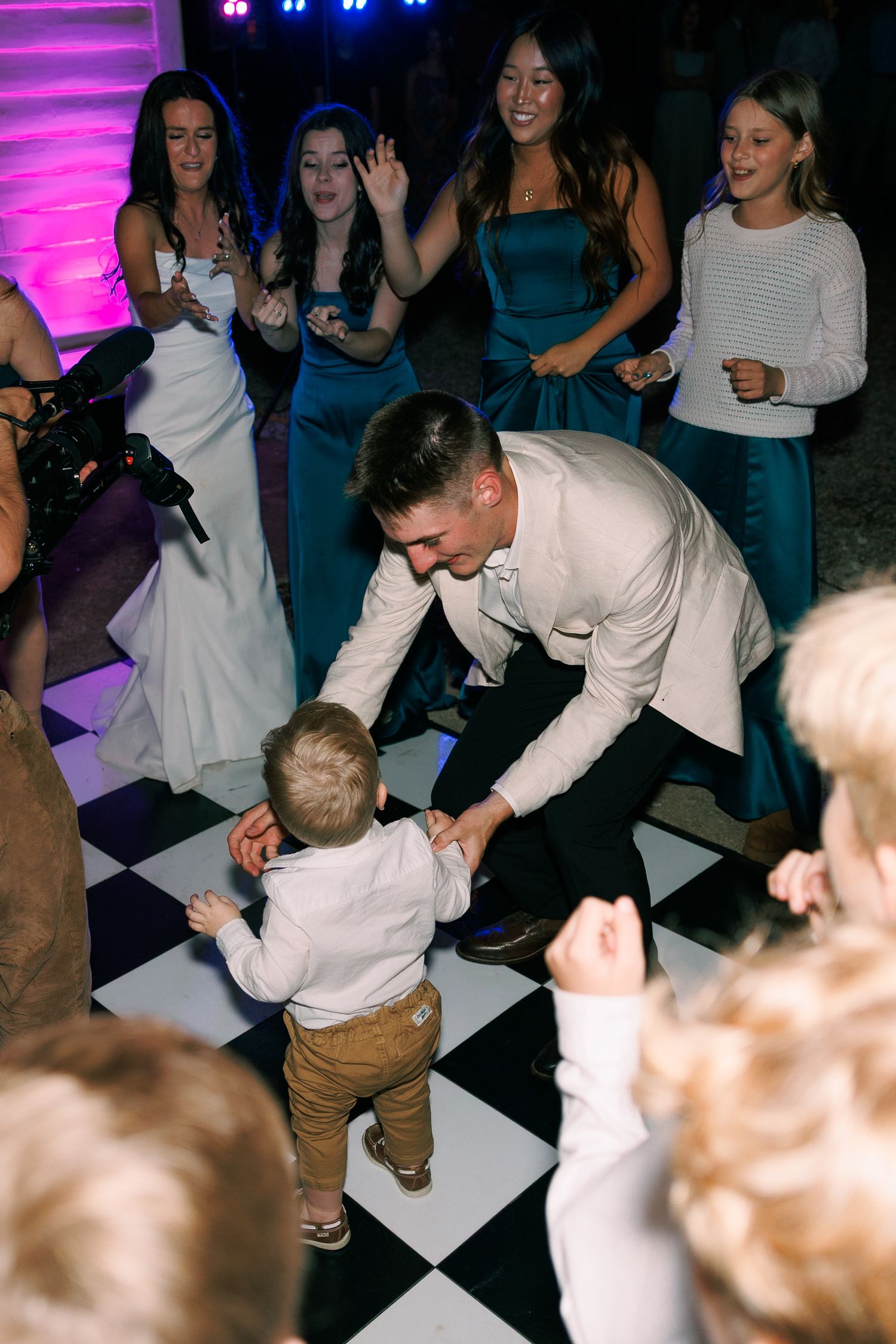 Lively dance floor scene with checkerboard pattern under purple lighting at wedding reception.