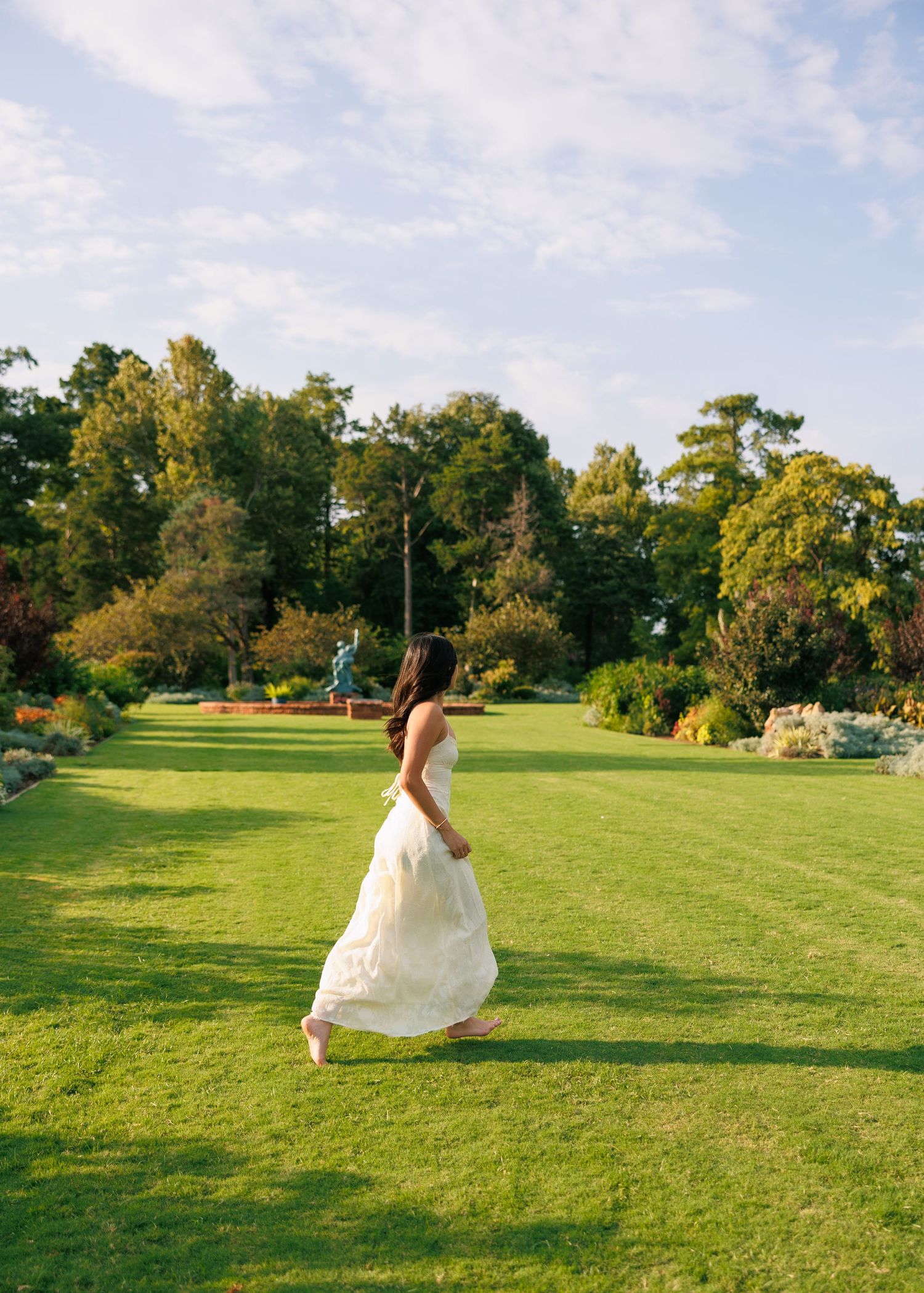 A white dress twirls on a manicured lawn with trees in the background during golden hour.