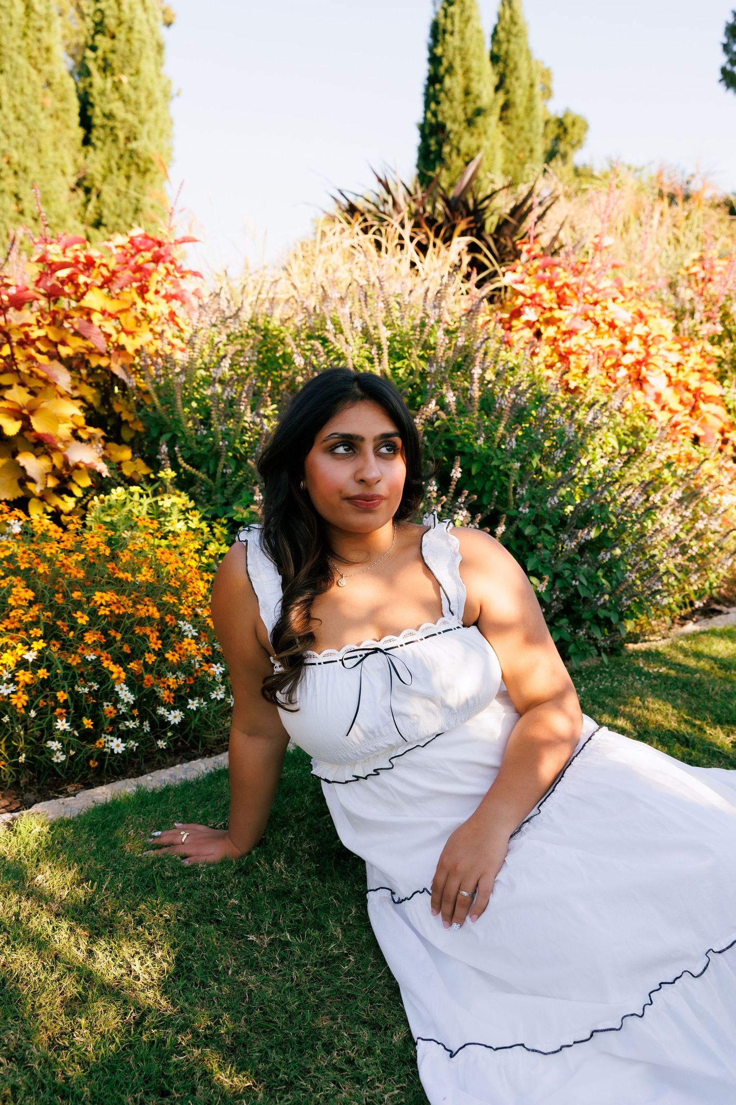 Summer garden photoshoot featuring white dress against colorful flower backdrop.