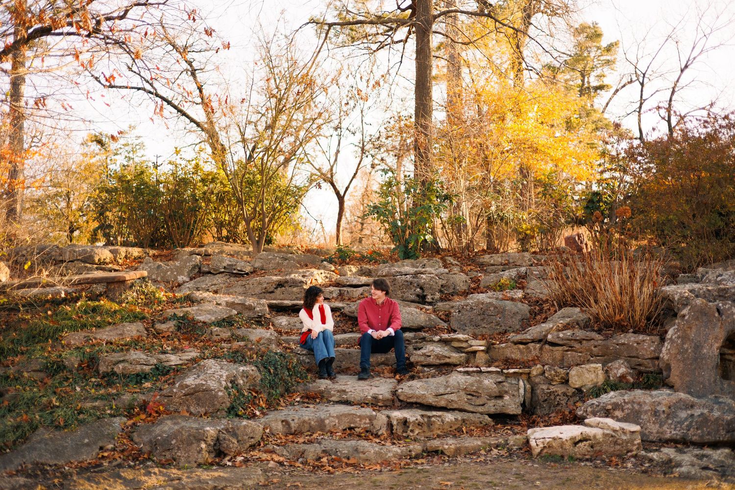 Two people sitting on rocky terrain in a park during autumn sunset.