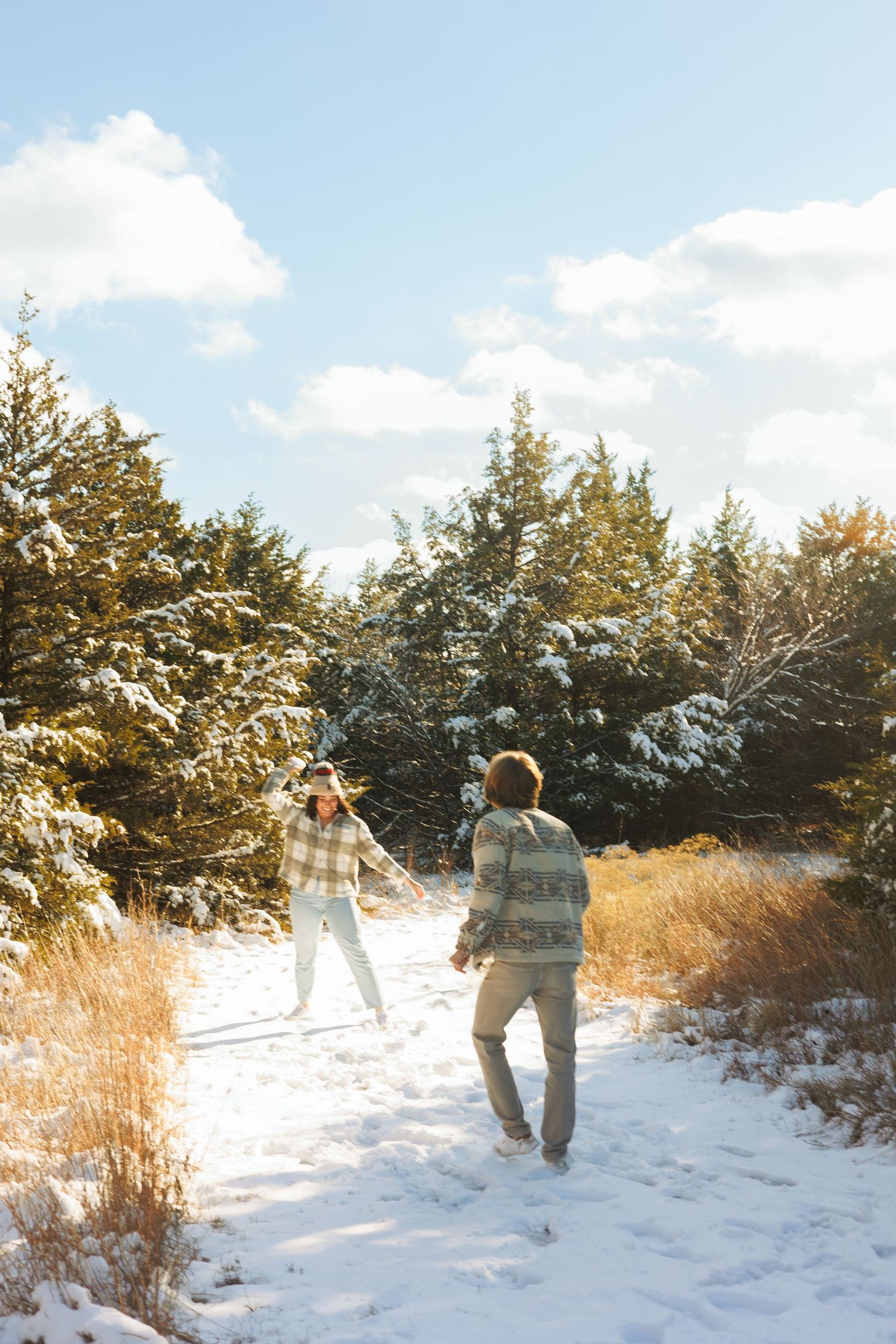 Two people exploring a snow-covered trail surrounded by winter evergreens.