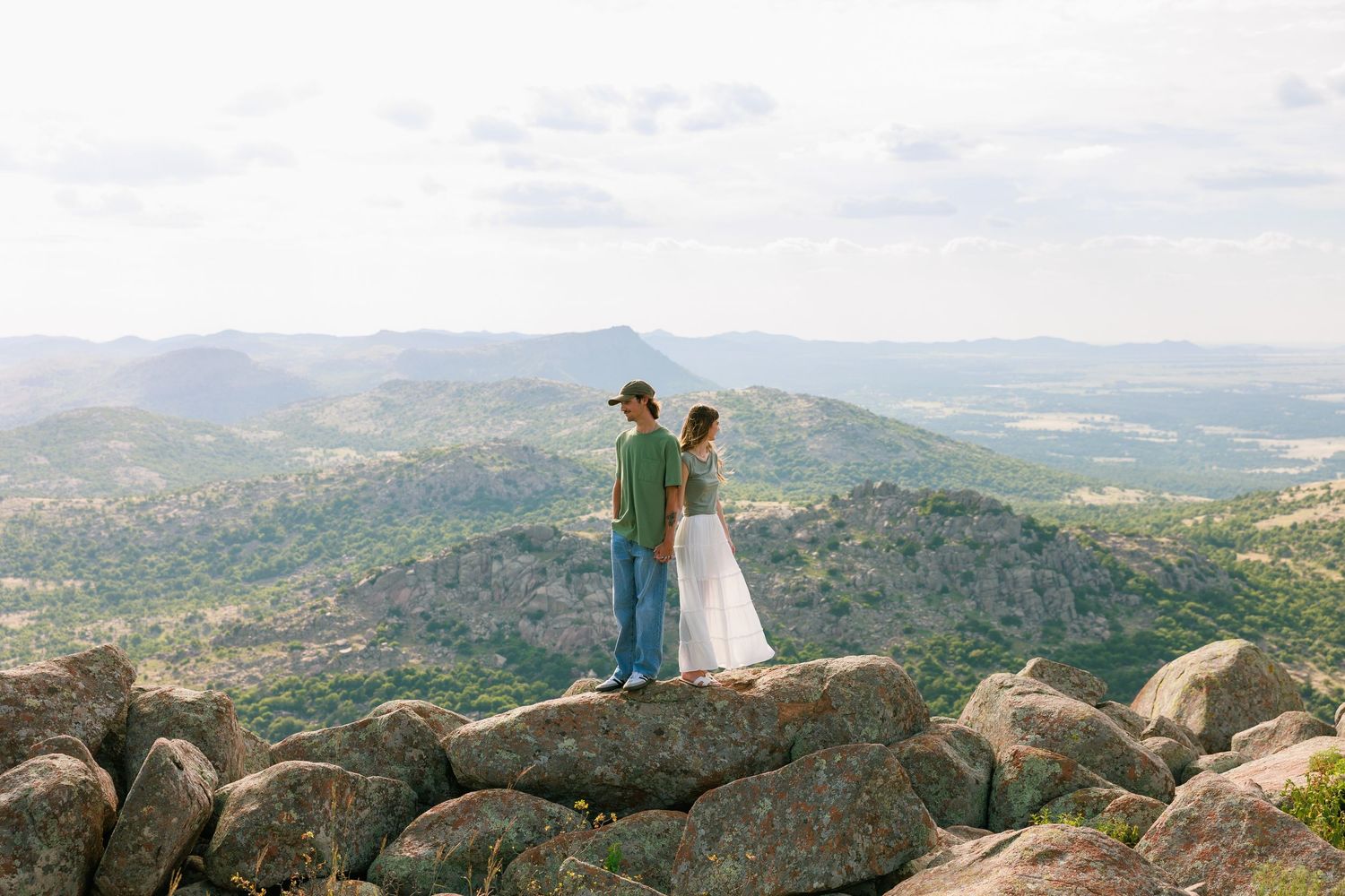 Two figures silhouetted against dramatic mountain vista on rocky overlook.