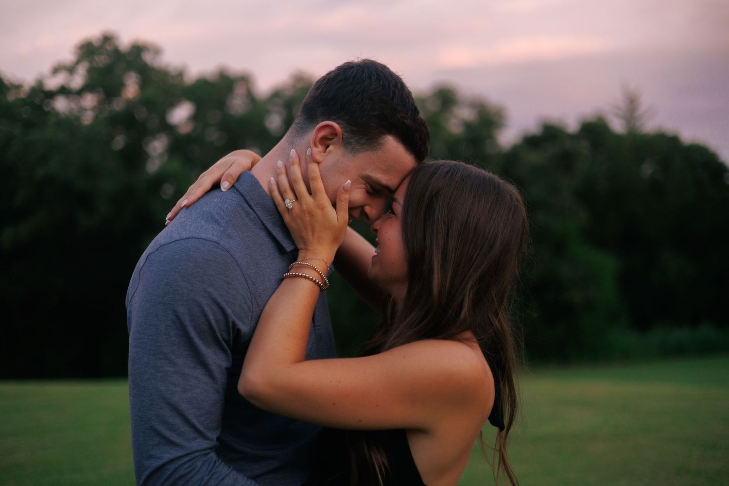 A romantic sunset moment in a grassy park with trees silhouetted in the background.