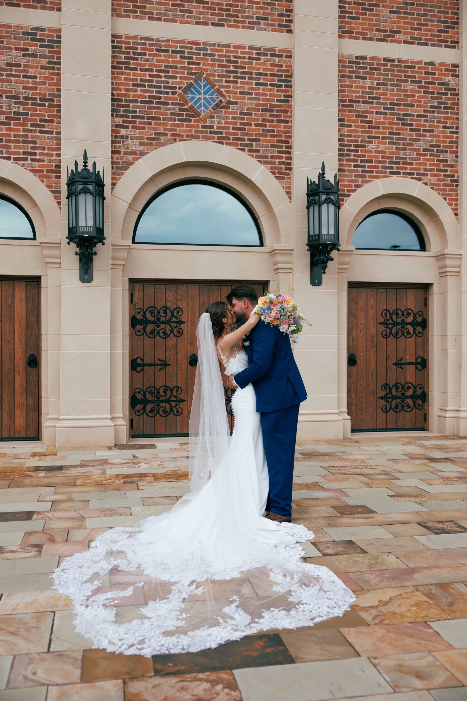 Dramatic cathedral-length wedding dress train displayed against brick and stone church architecture.