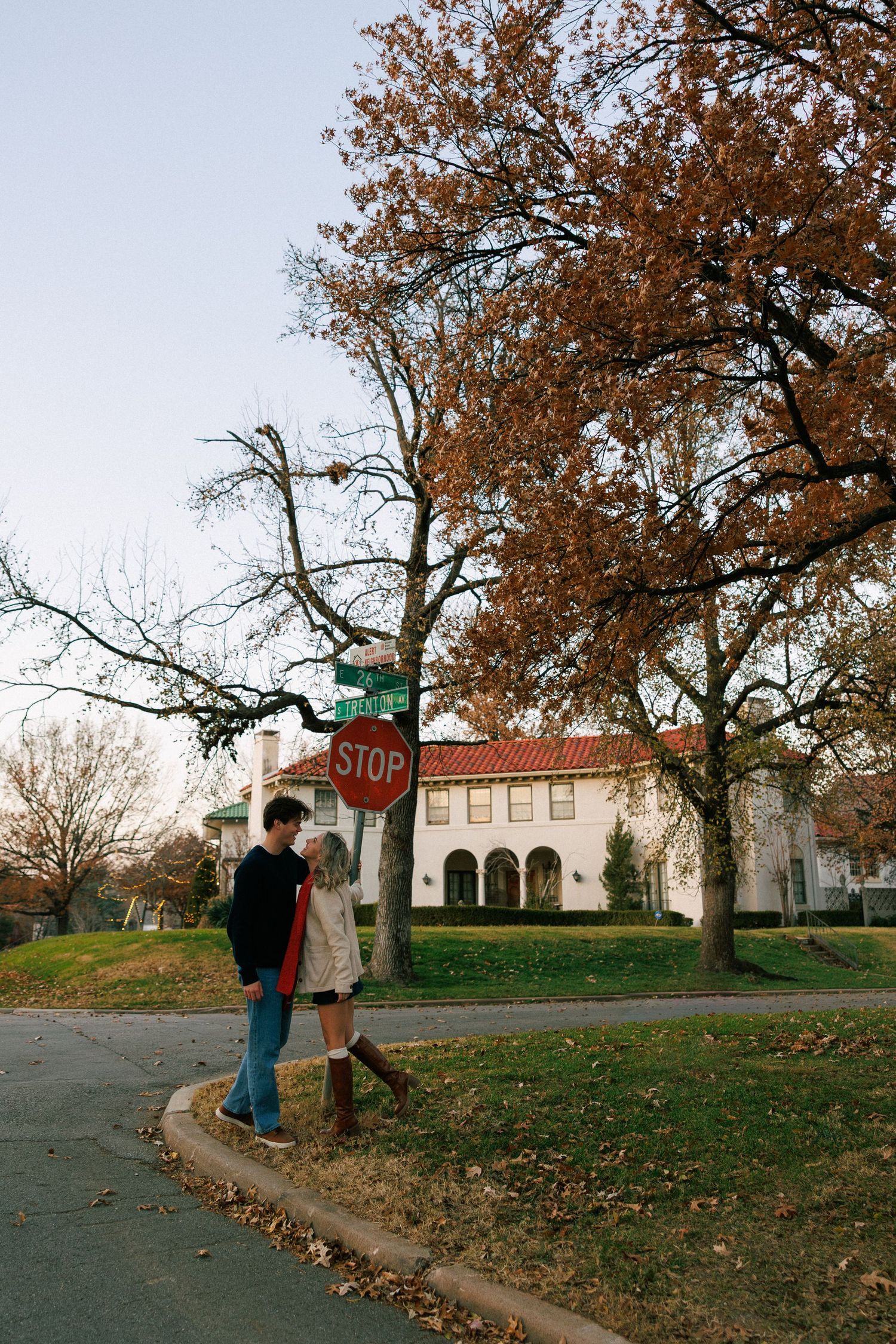 A couple stands near a stop sign on an autumn day with a Spanish-style building in the background.