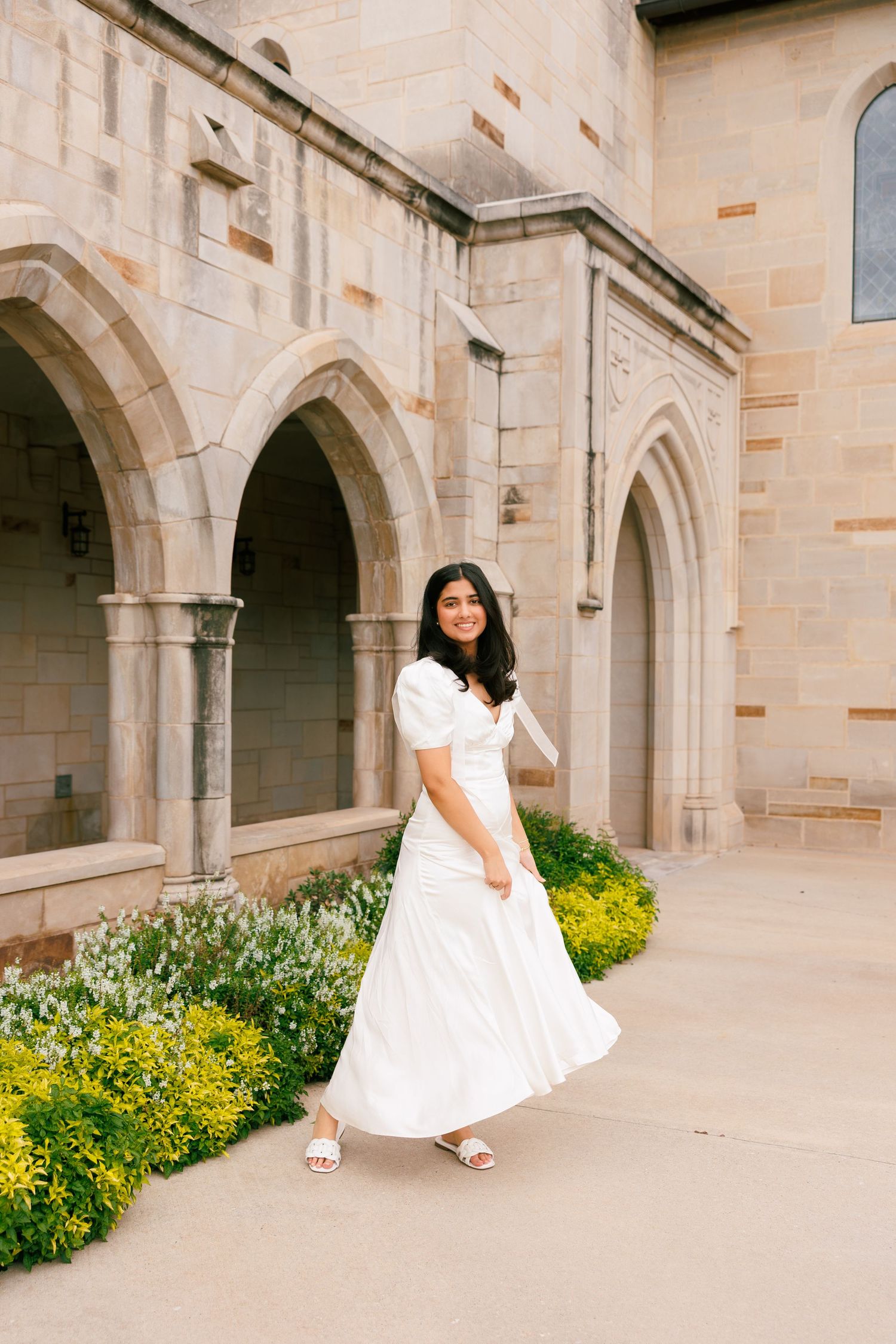 White dress portraits in an elegant stone archway with yellow flowers blooming below.
