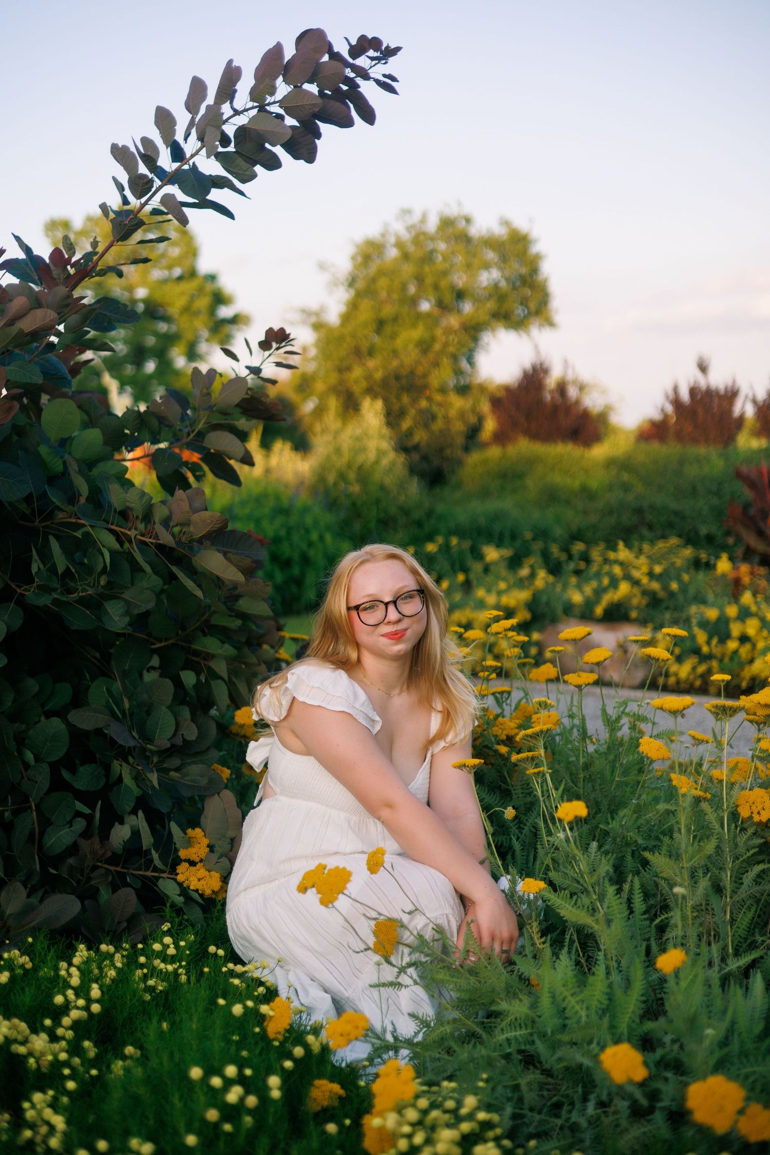 White dress portrait among blooming yellow wildflowers in a garden setting.
