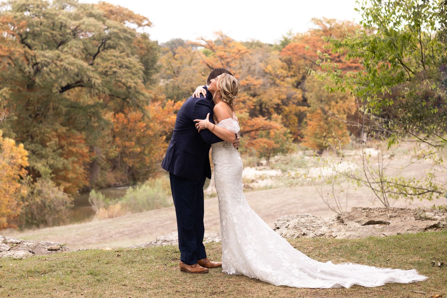 A couple embraces in a romantic autumn setting with golden fall foliage in the background.