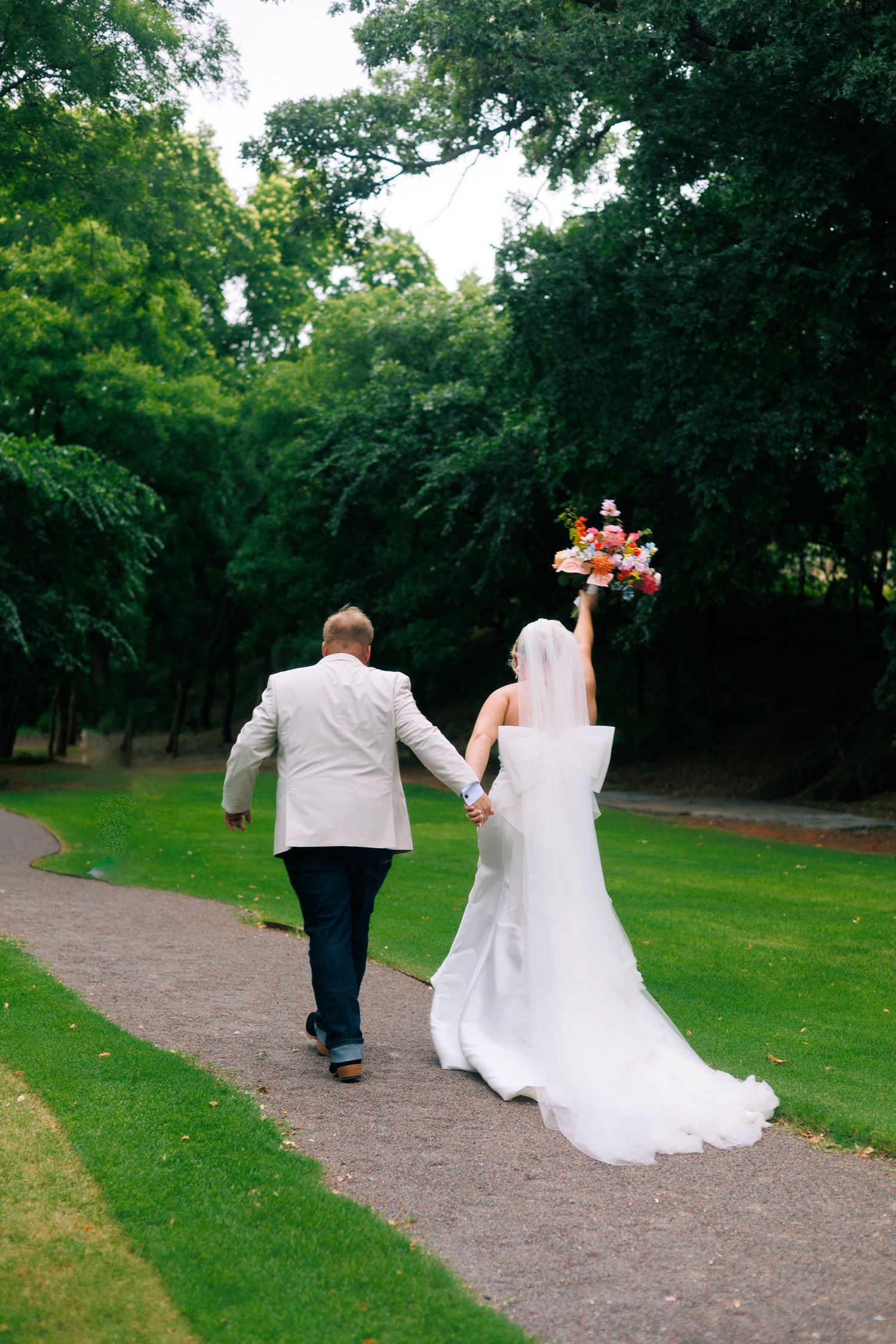 A couple walks down a winding path surrounded by lush greenery.