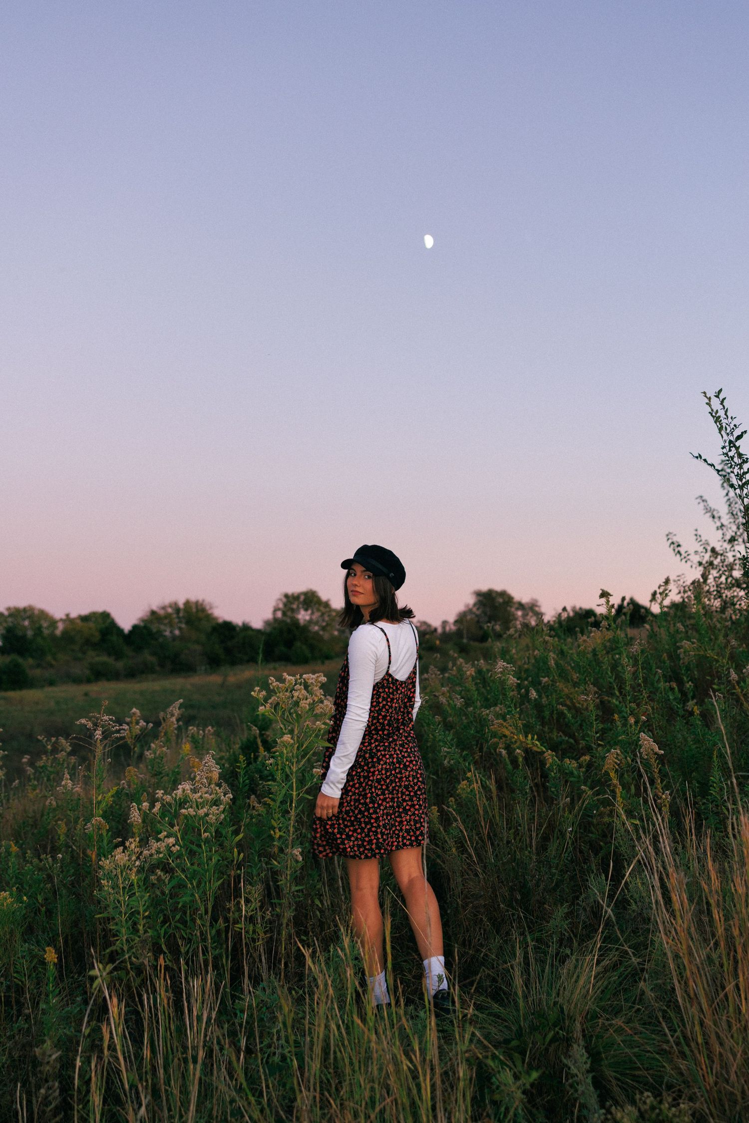 A twilight photoshoot in a meadow with tall grass and a moon visible in the dusky sky.