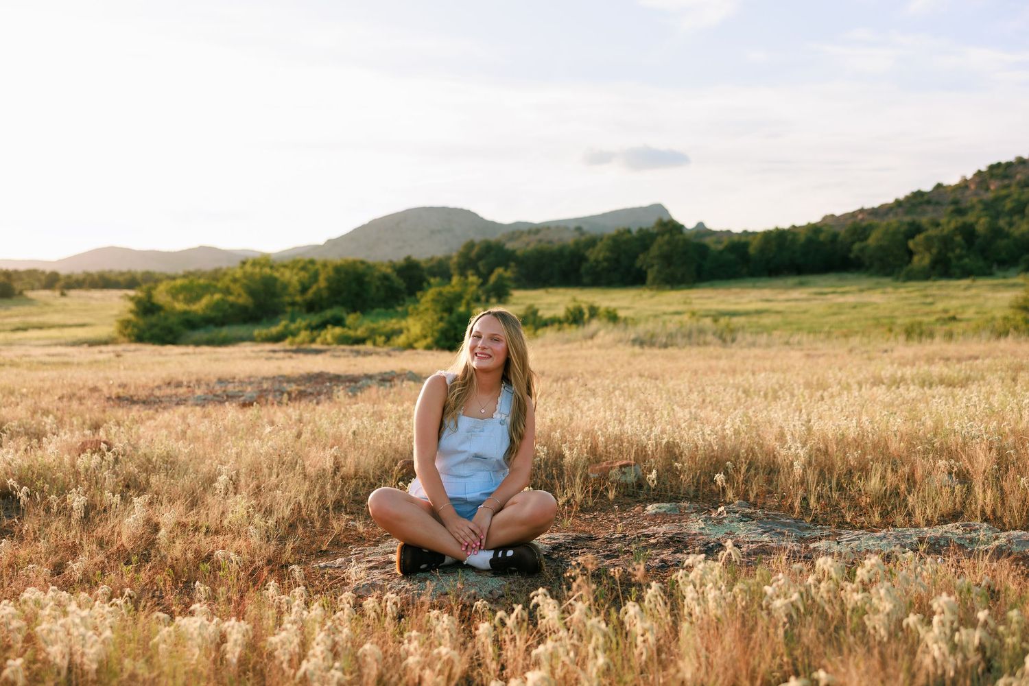 Someone sitting in a field with mountains and rolling hills in the background.