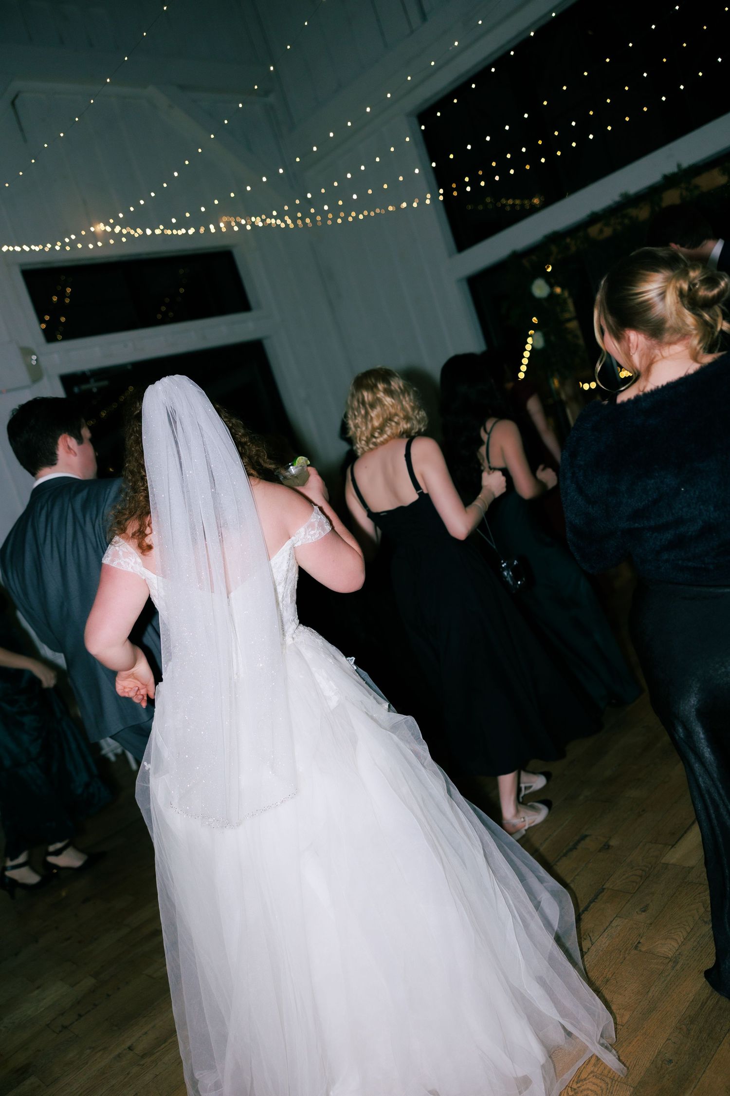 Wedding reception dance floor with string lights overhead and guests dancing in formal attire.