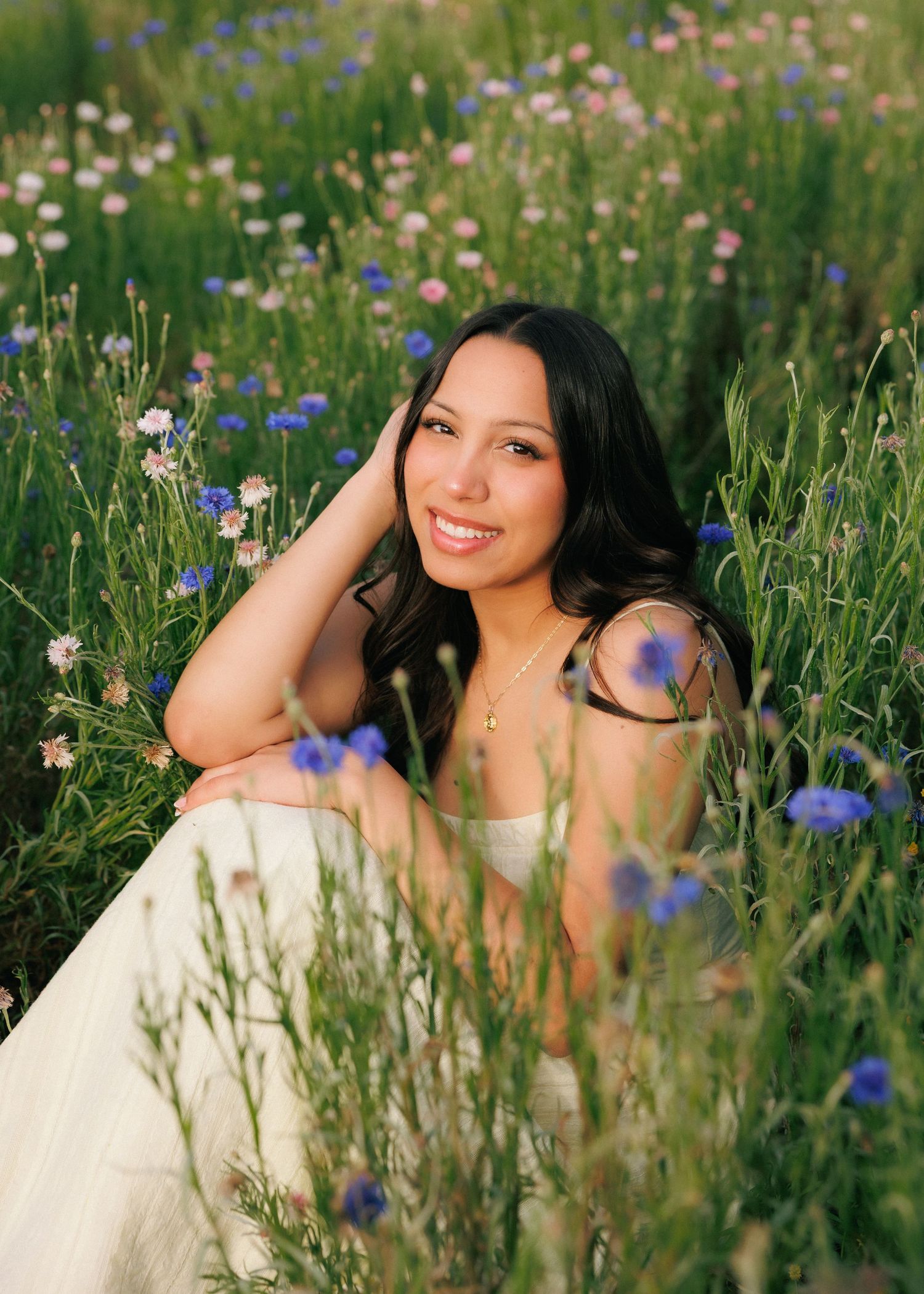 Young woman in white dress smiling among colorful wildflowers in a sunny meadow.