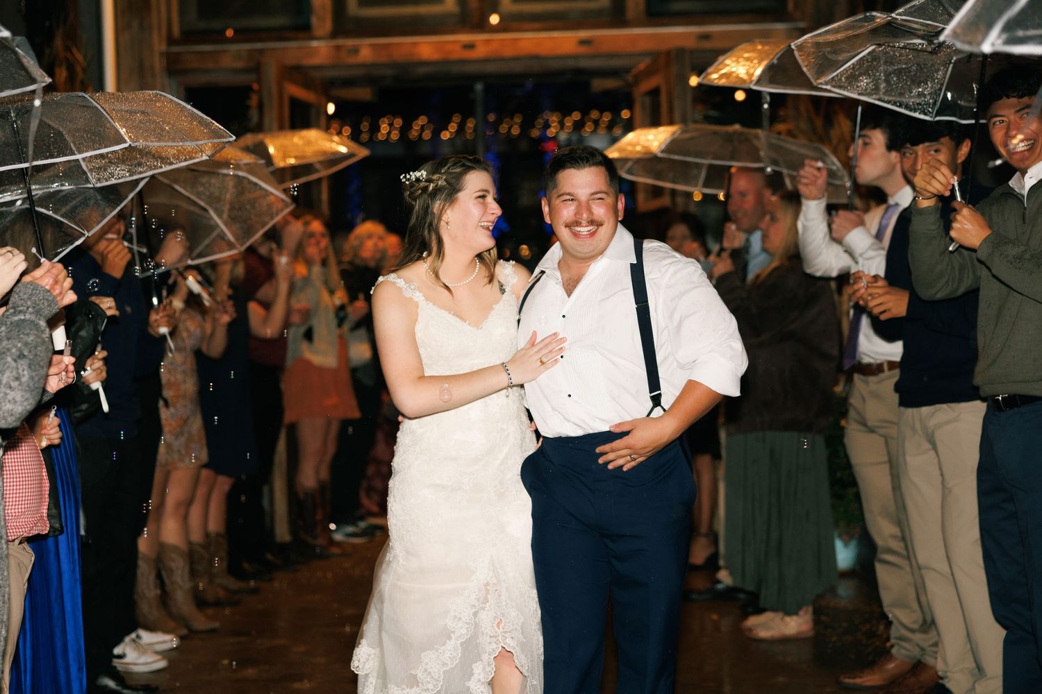 Wedding guests dance under clear umbrellas at outdoor evening reception.