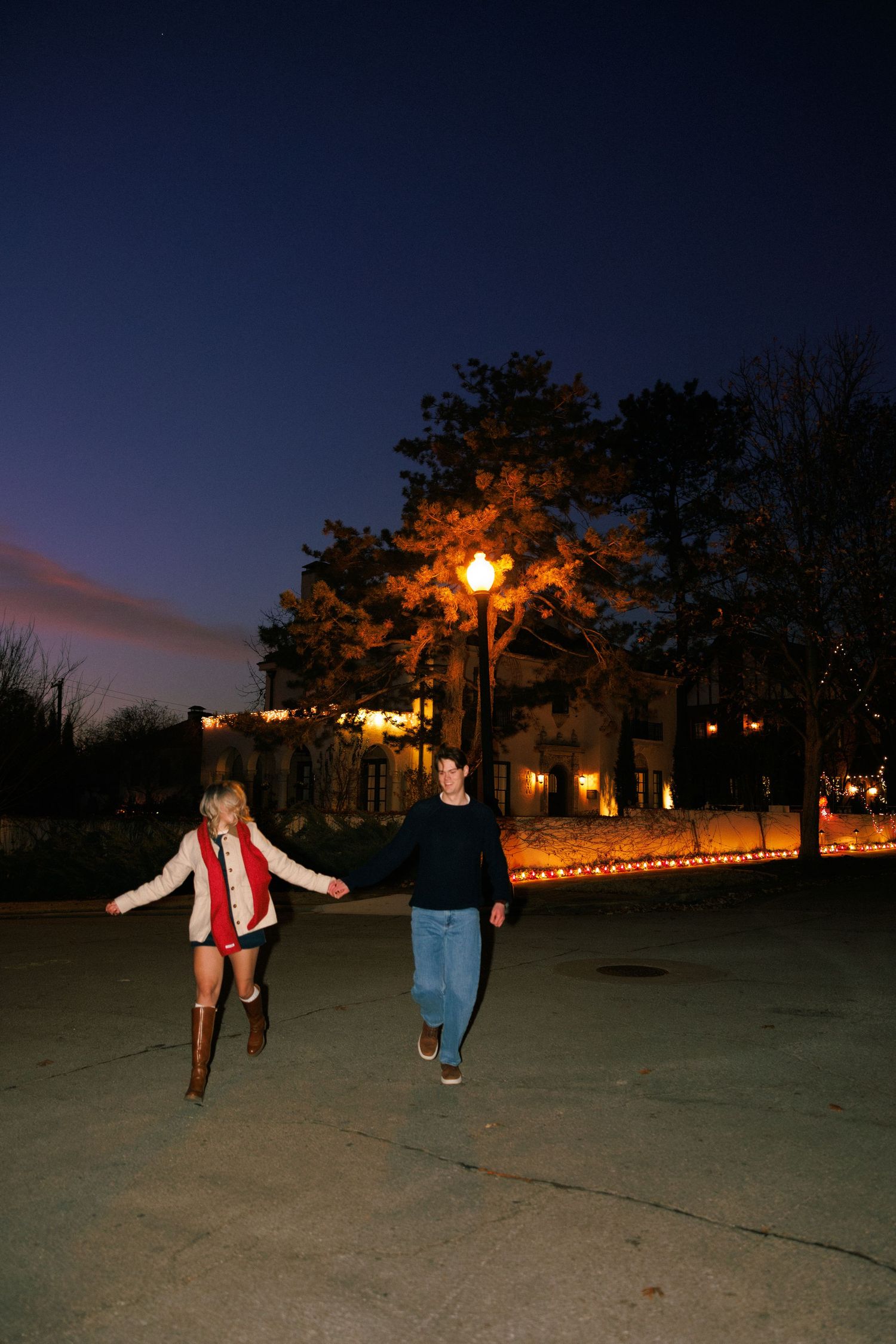 Two people walking together at dusk with illuminated buildings in the background.