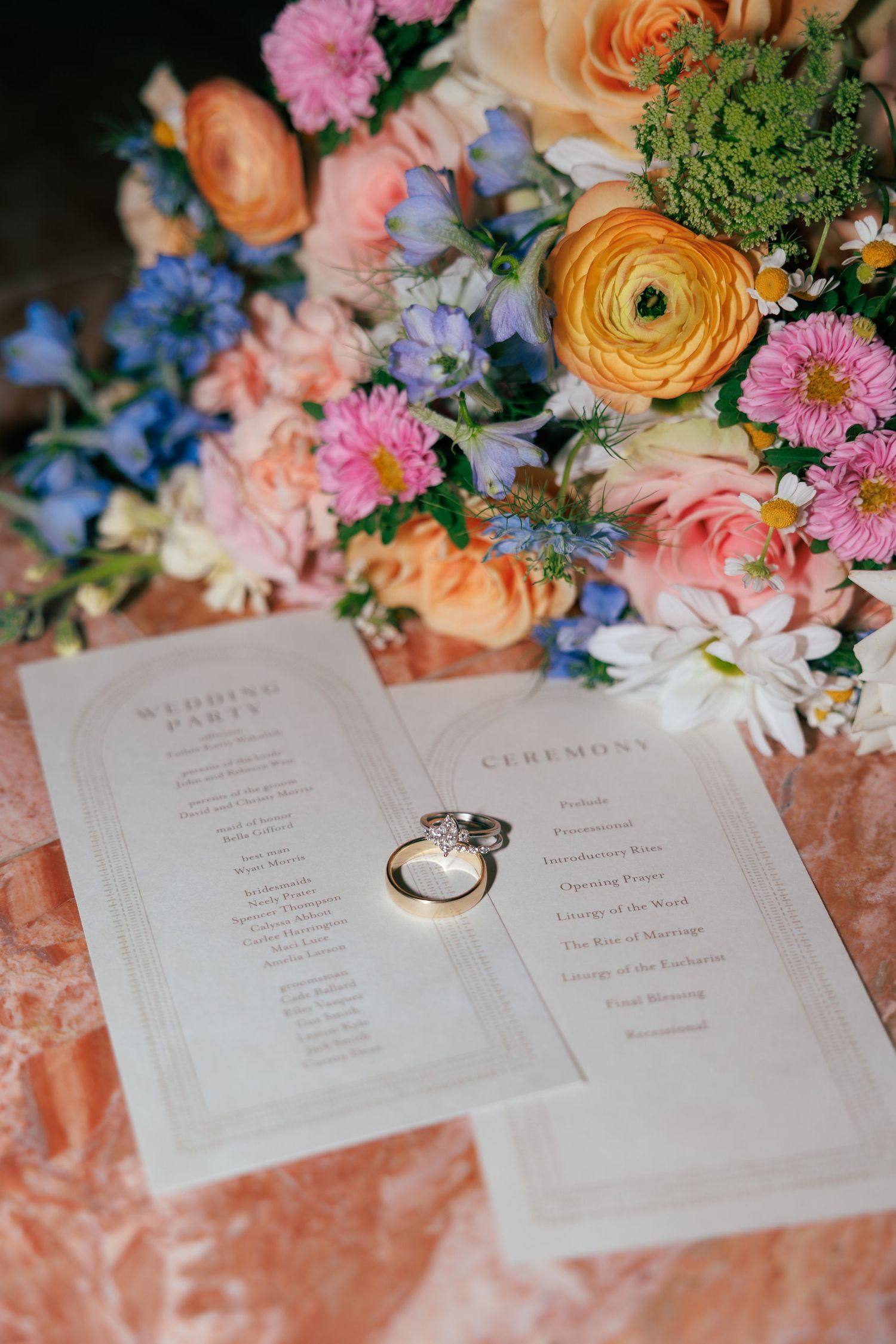 Wedding program and rings displayed with colorful pink, orange and blue floral arrangements.