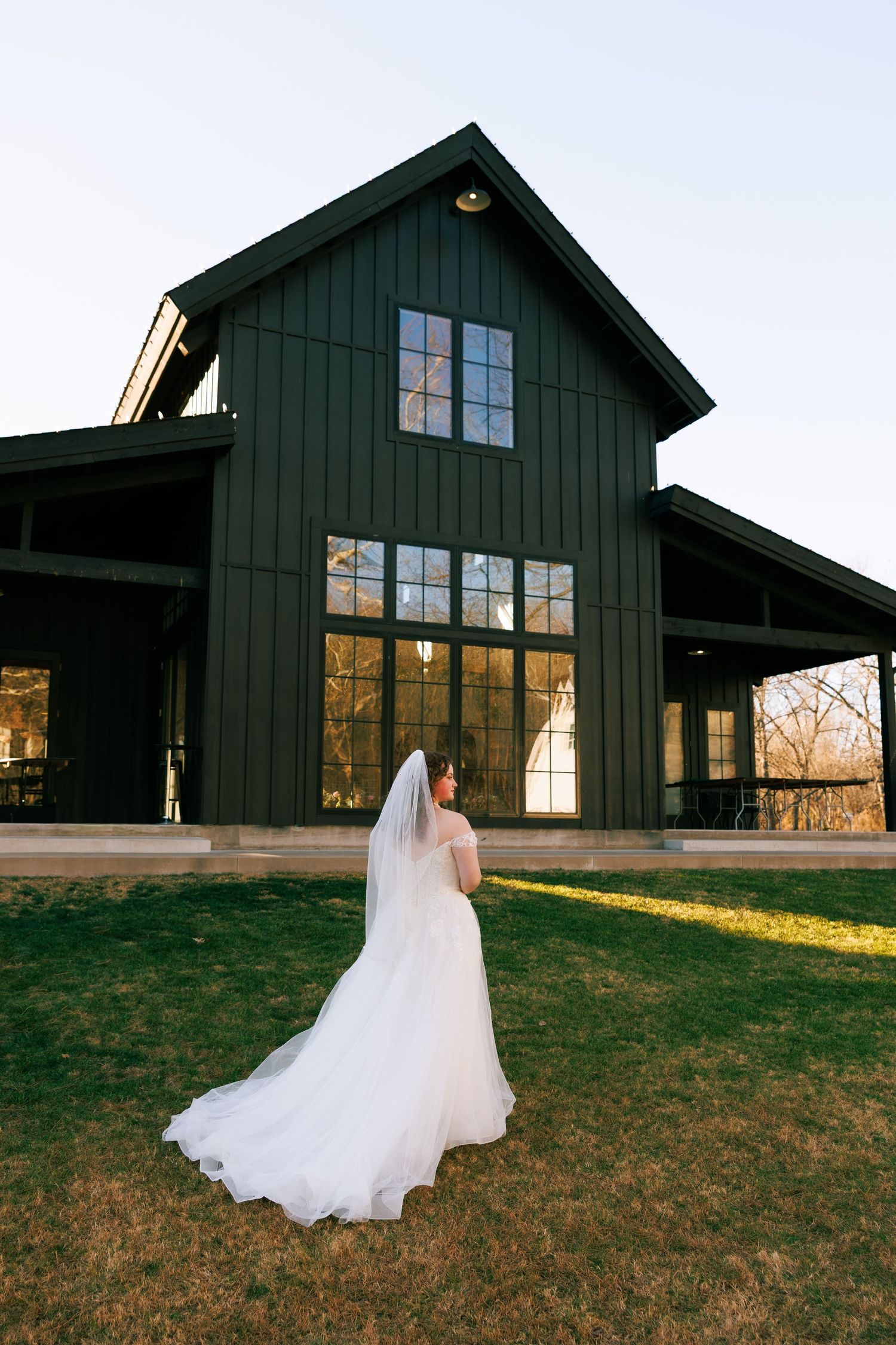 Modern black barn wedding venue exterior with white wedding dress in foreground during golden hour.