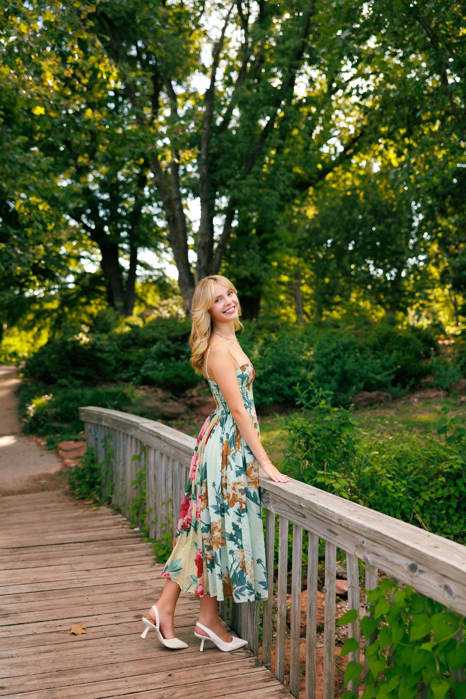 A floral dress catches the sunlight on a wooden bridge surrounded by lush greenery.