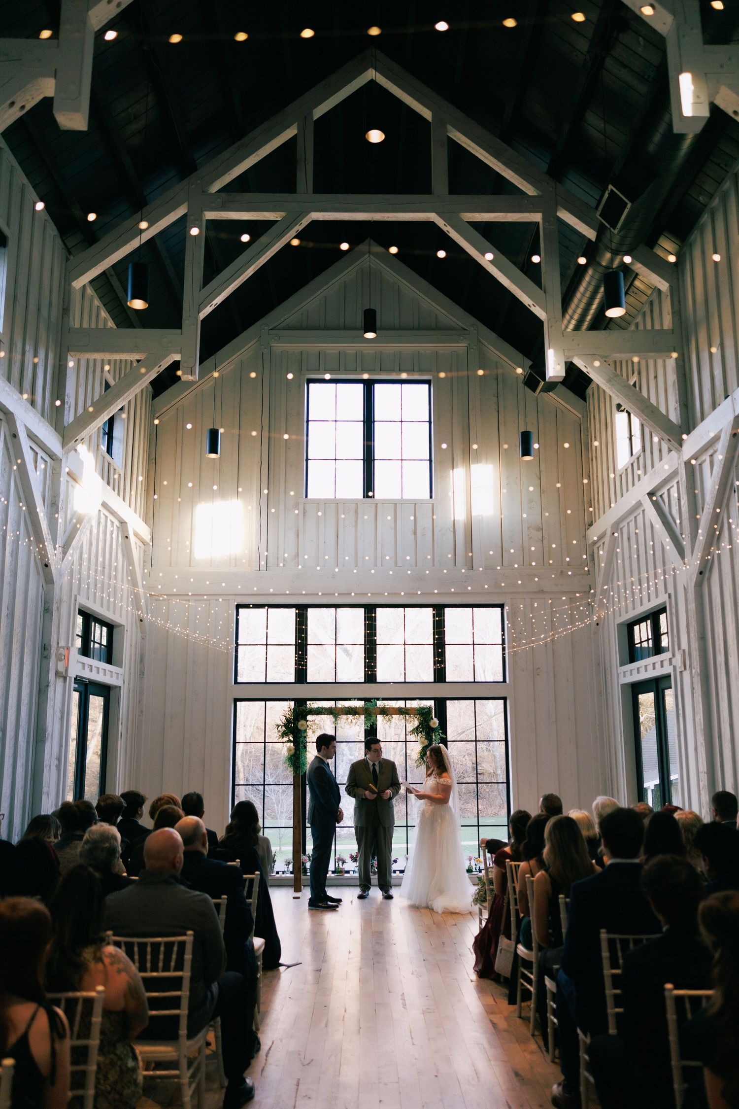 Elegant white wedding ceremony venue with vaulted ceilings, string lights and rows of chairs.