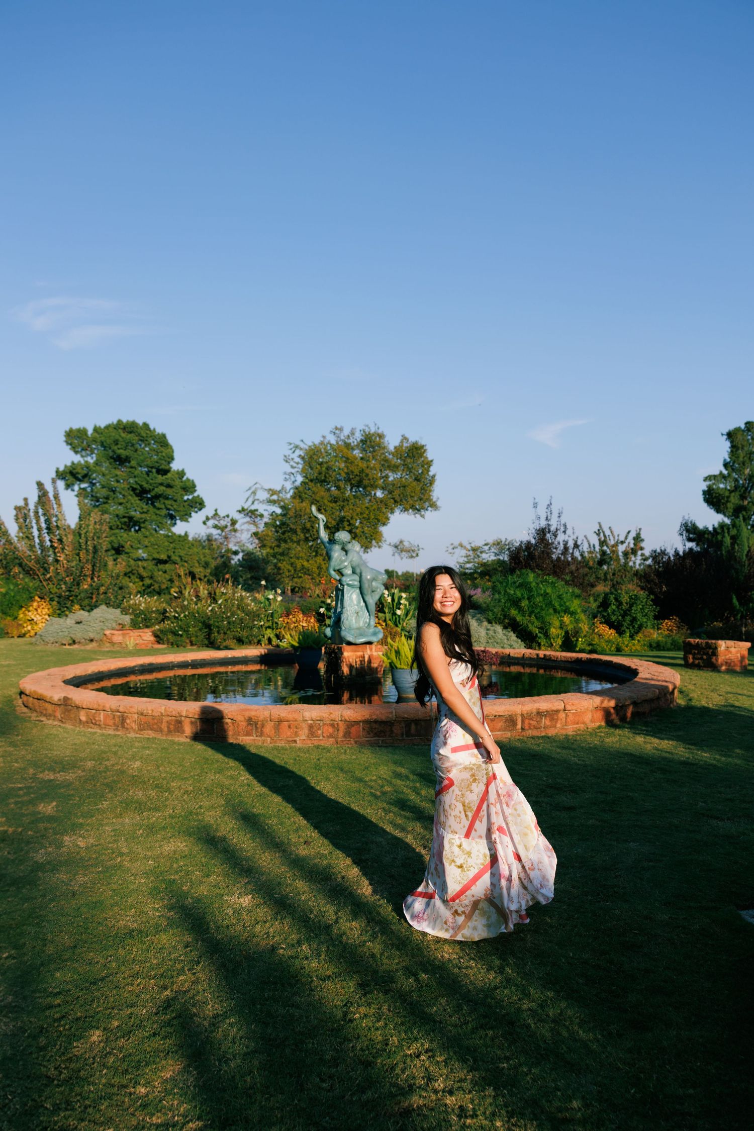 A floral dress twirls in a garden setting with a circular brick fountain feature.