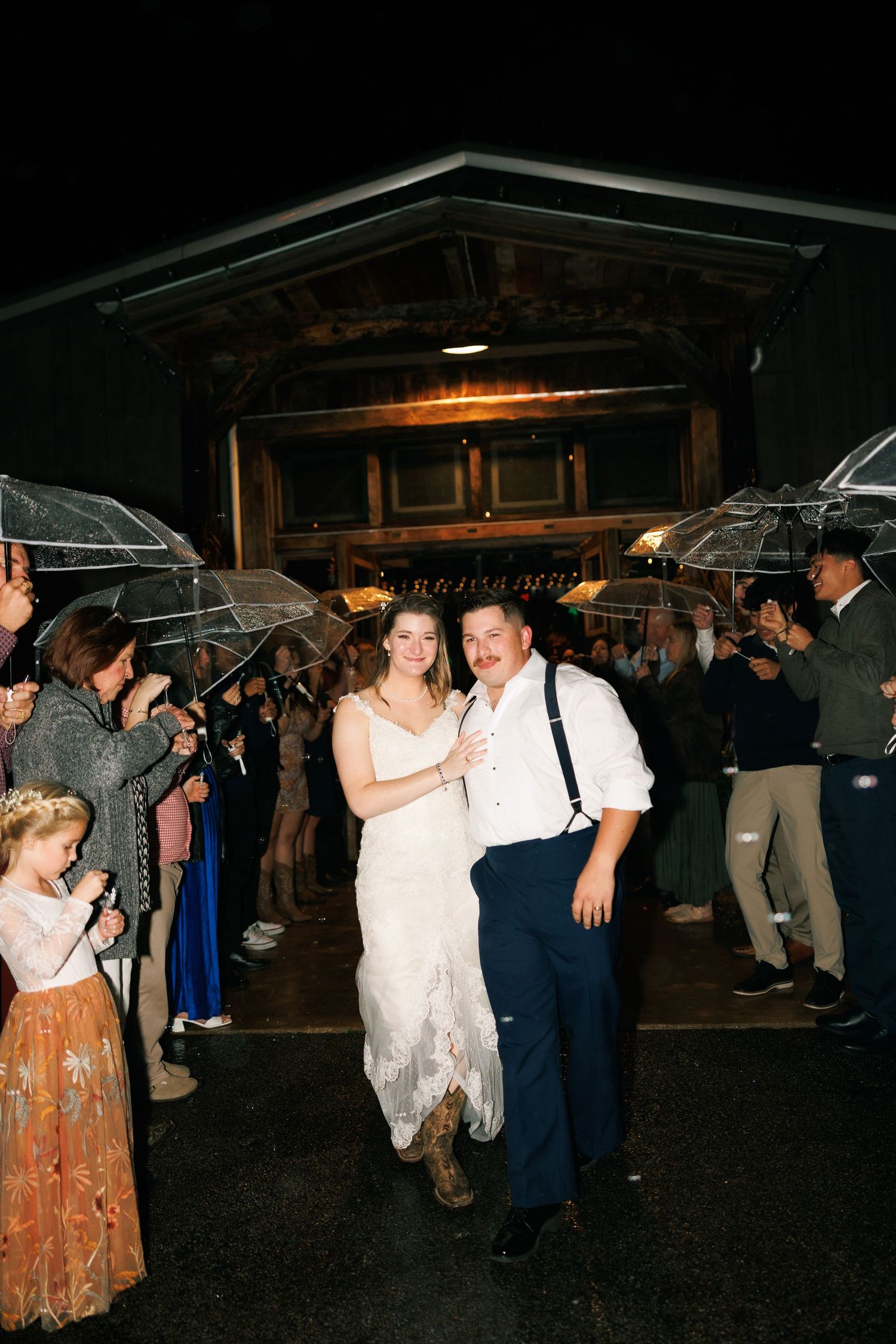 Wedding guests dance under clear umbrellas during an evening outdoor reception celebration.