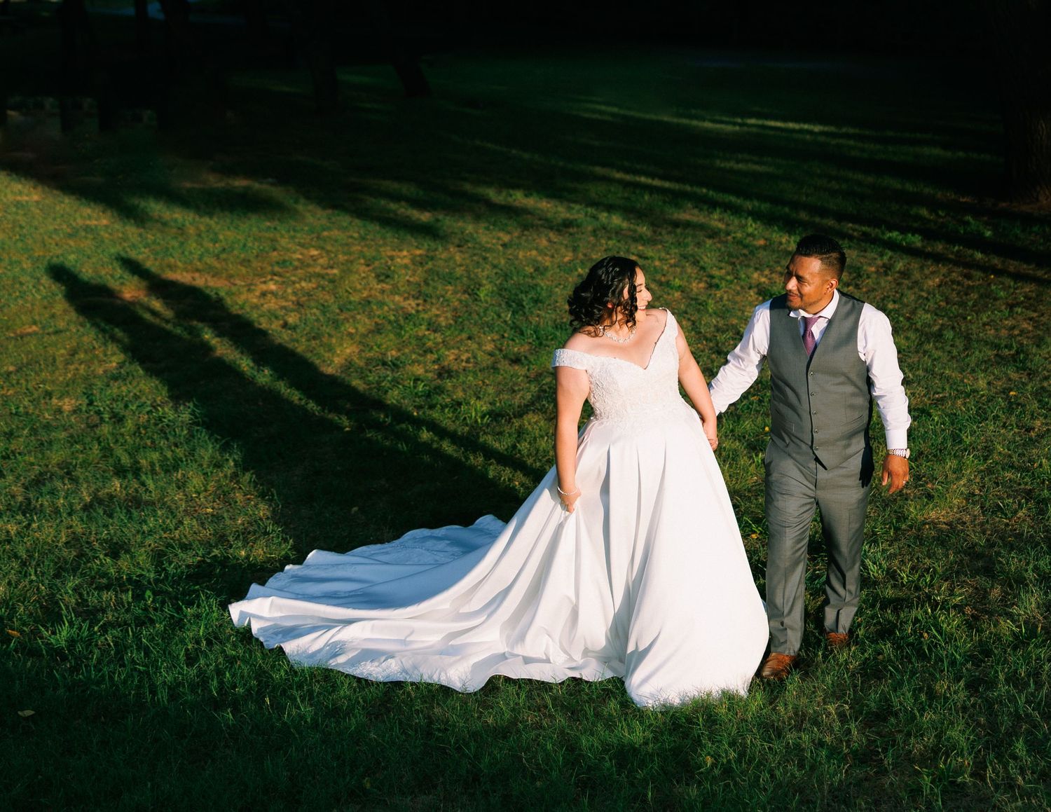 Wedding couple poses dramatically on grassy hillside at sunset.
