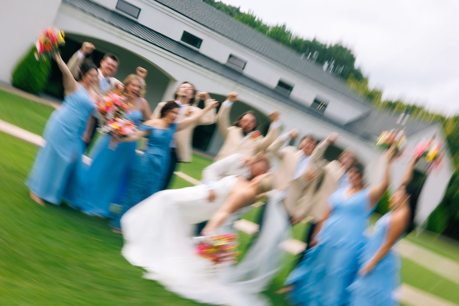 Wedding party celebration captured in motion on a grassy lawn.