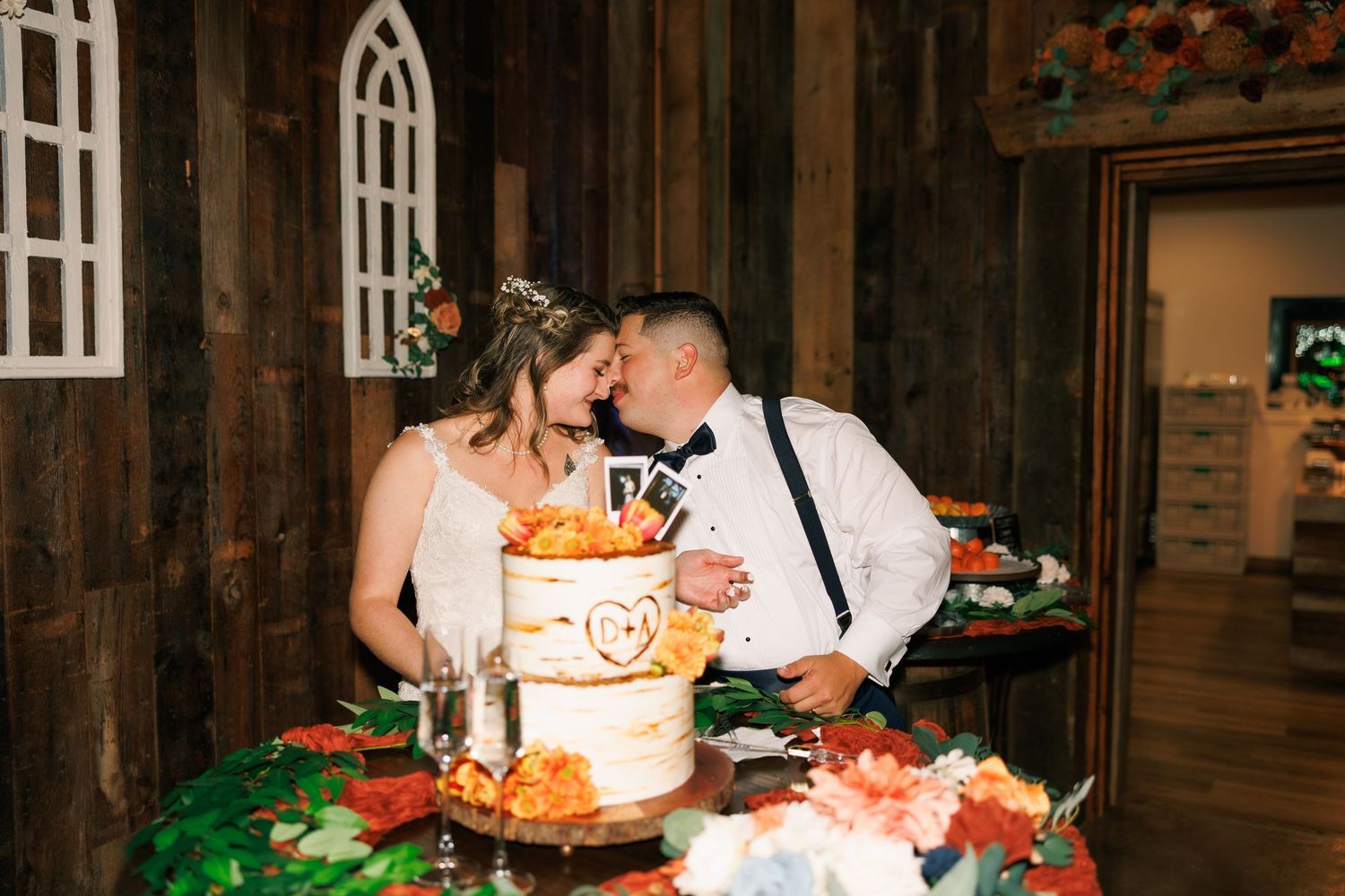 Couple cutting their orange-decorated wedding cake in rustic wooden venue.