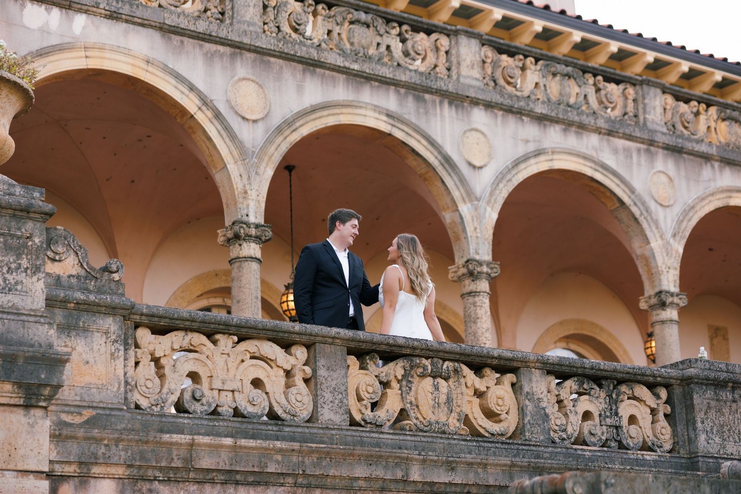 Wedding couple photographed on a historic Philbrook Museum balcony with ornate architectural details.