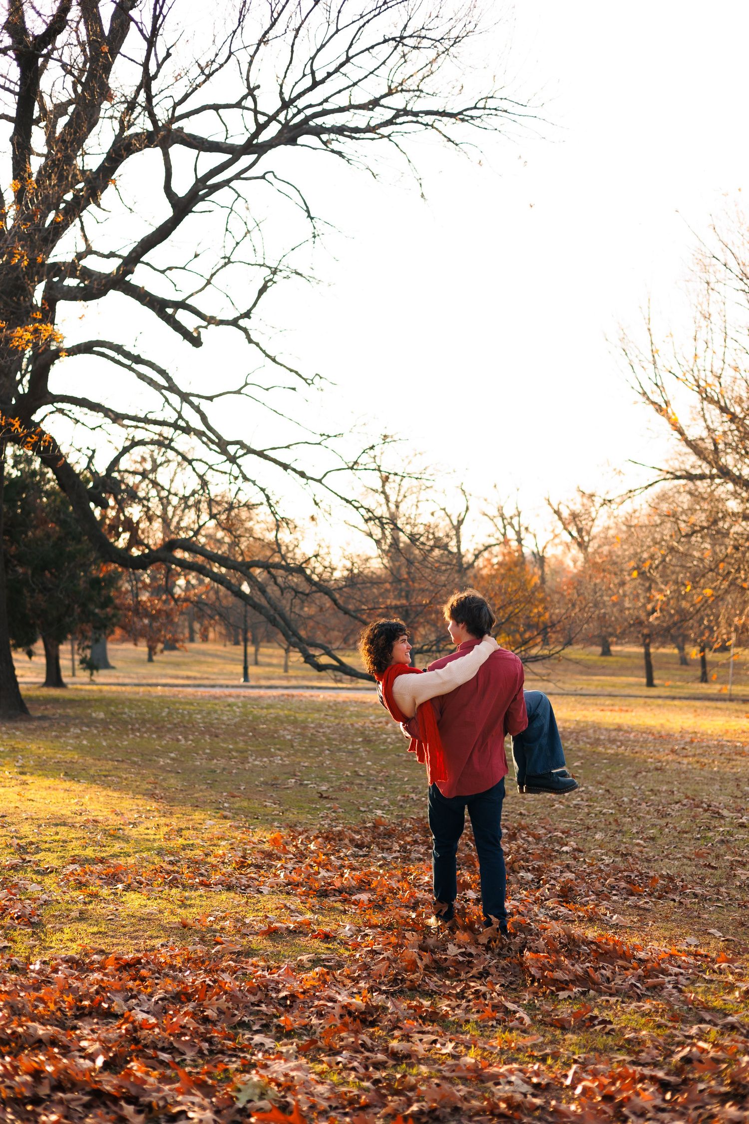 Two people enjoying a playful moment among fallen leaves in an autumn park.
