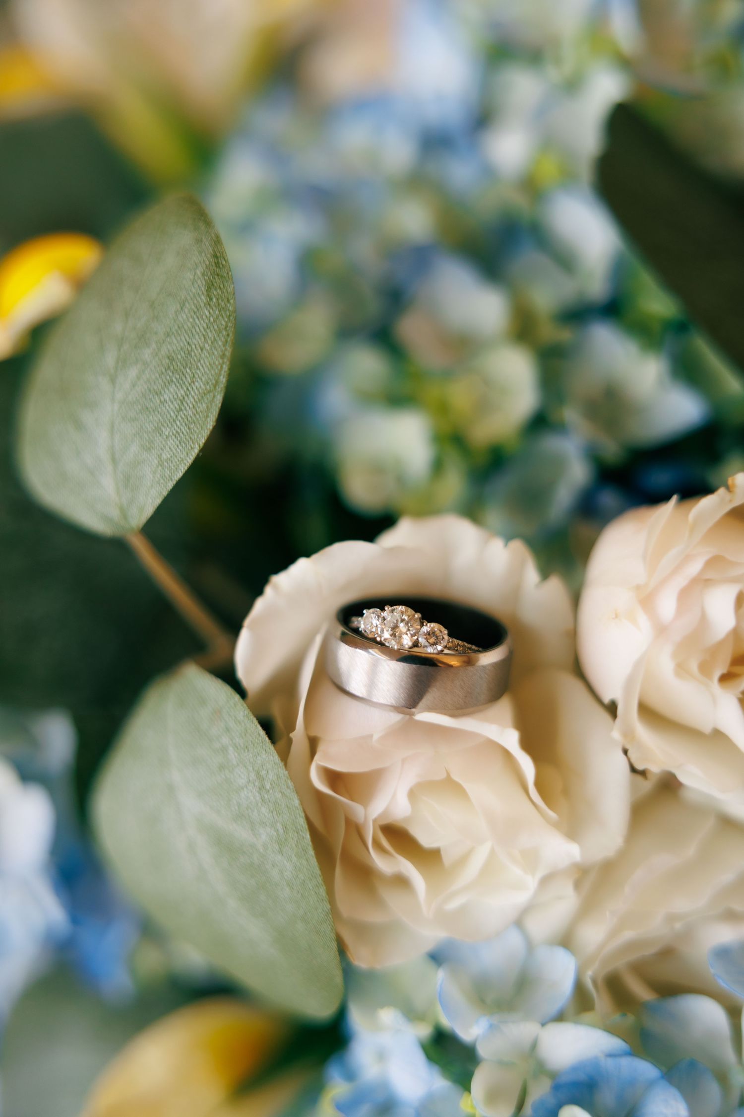Close-up of an engagement ring nestled among delicate cream roses and blue flowers.
