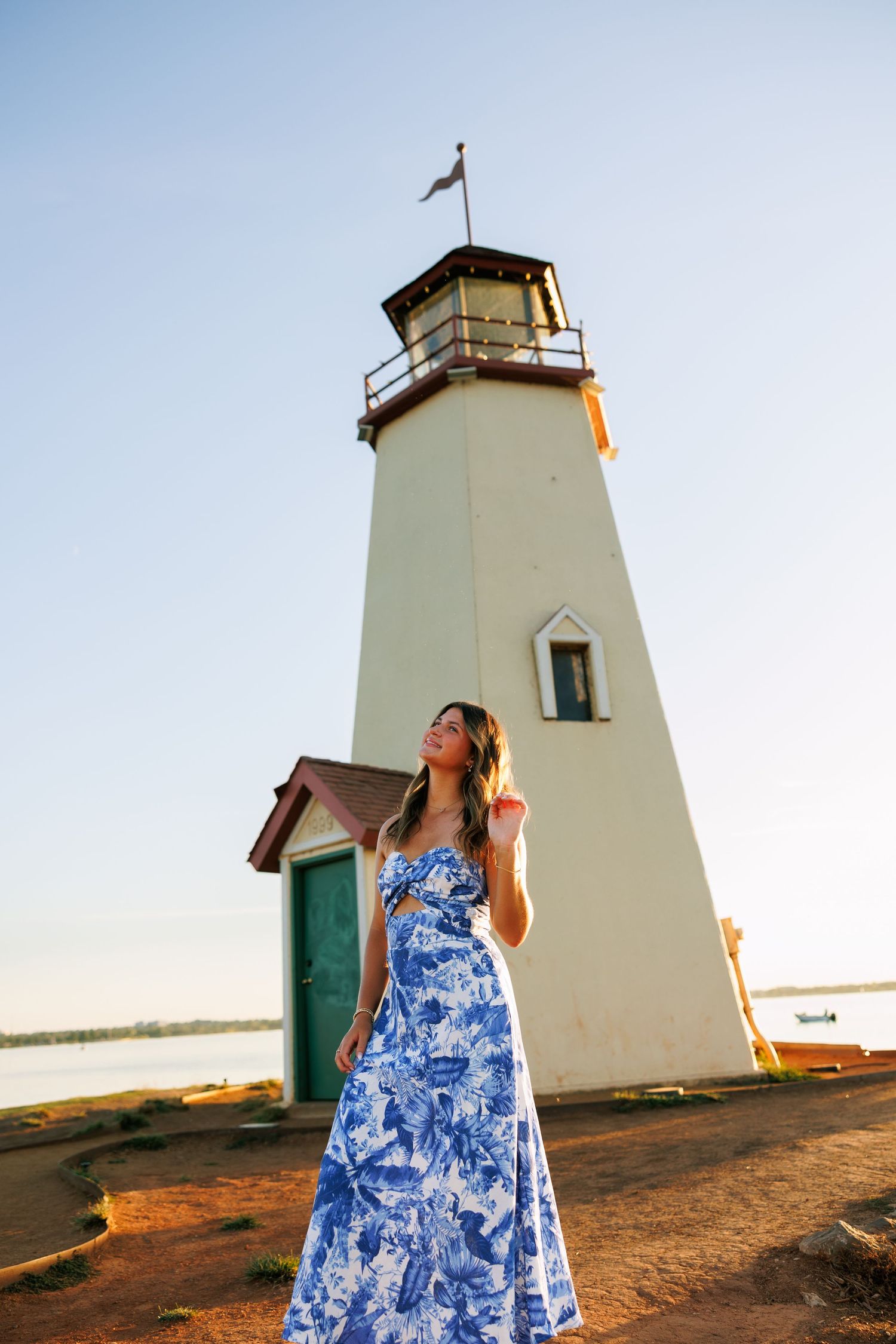 A blue and white floral maxi dress stands out against a classic white lighthouse backdrop at sunset.