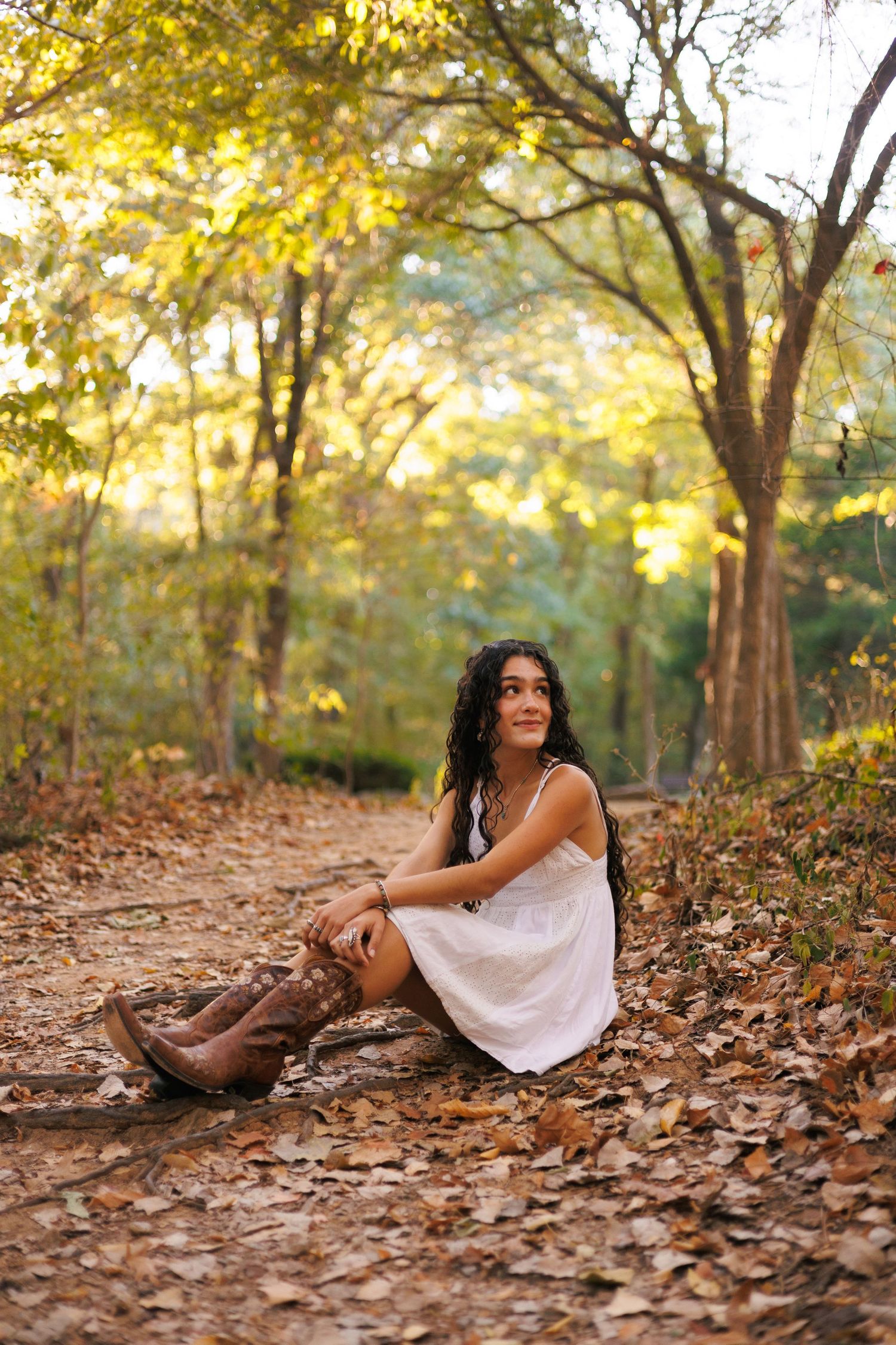 Artistic autumn portrait among fallen leaves with golden sunlight filtering through trees.