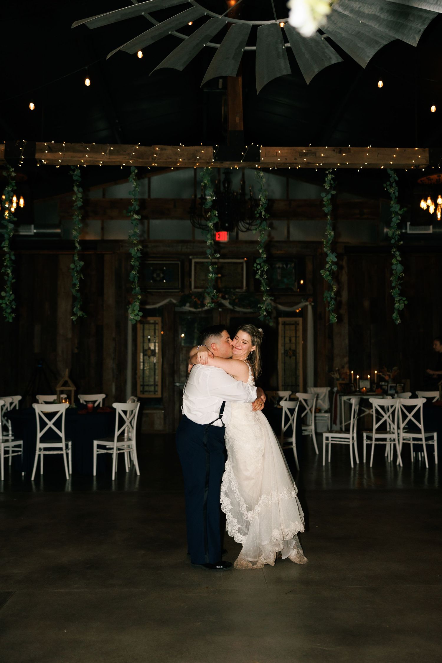First dance in rustic venue with string lights and wooden ceiling beams.