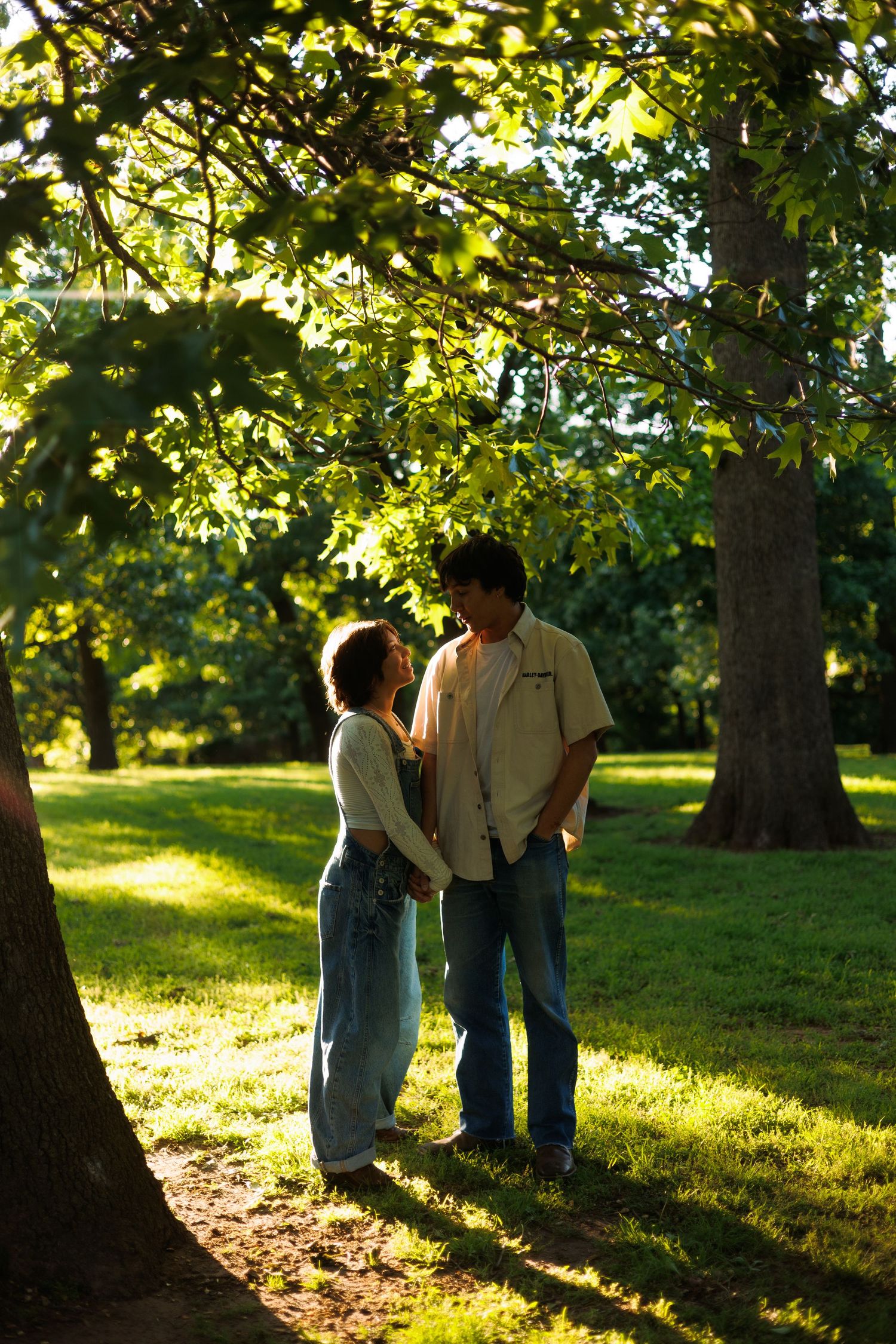 A couple shares a tender moment in a sun-drenched park setting.
