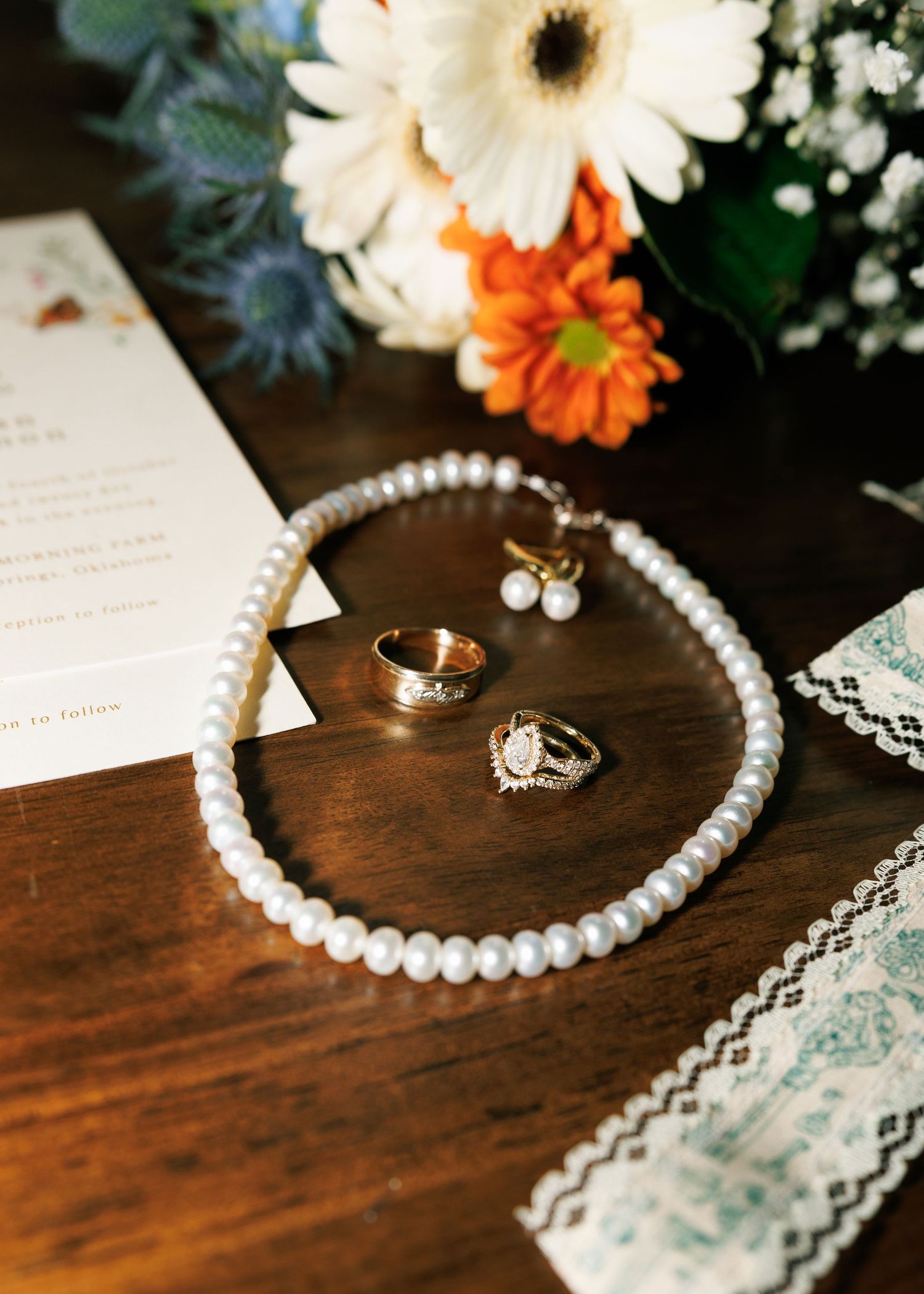 Wedding accessories including pearl necklace, rings, and flowers arranged on wooden surface.