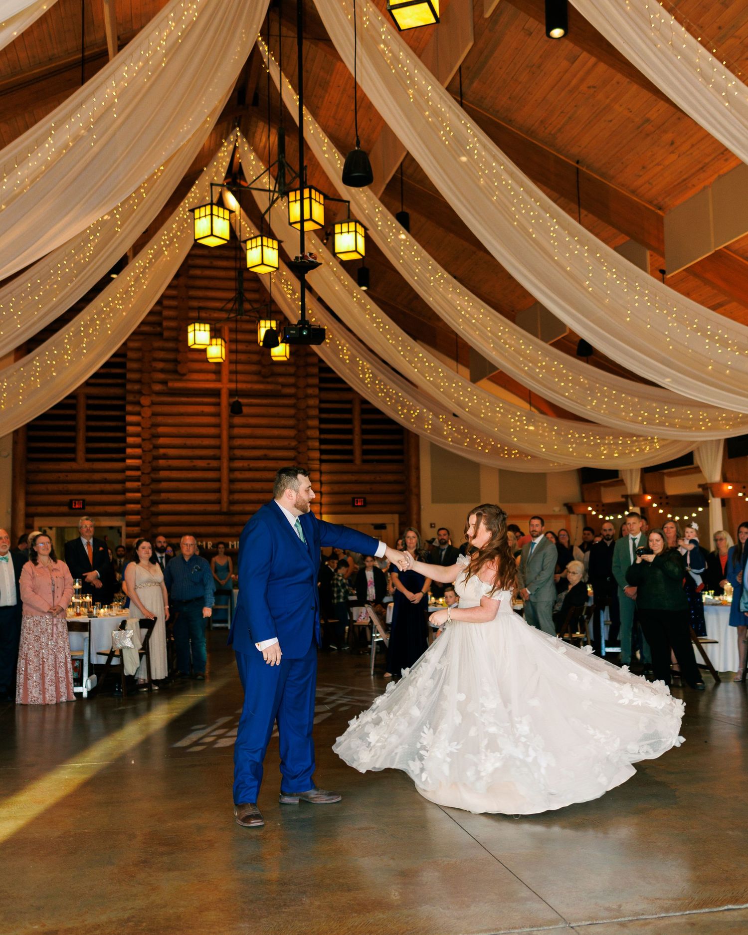 Wedding couple dancing under draped fabric and lanterns in a rustic reception venue.