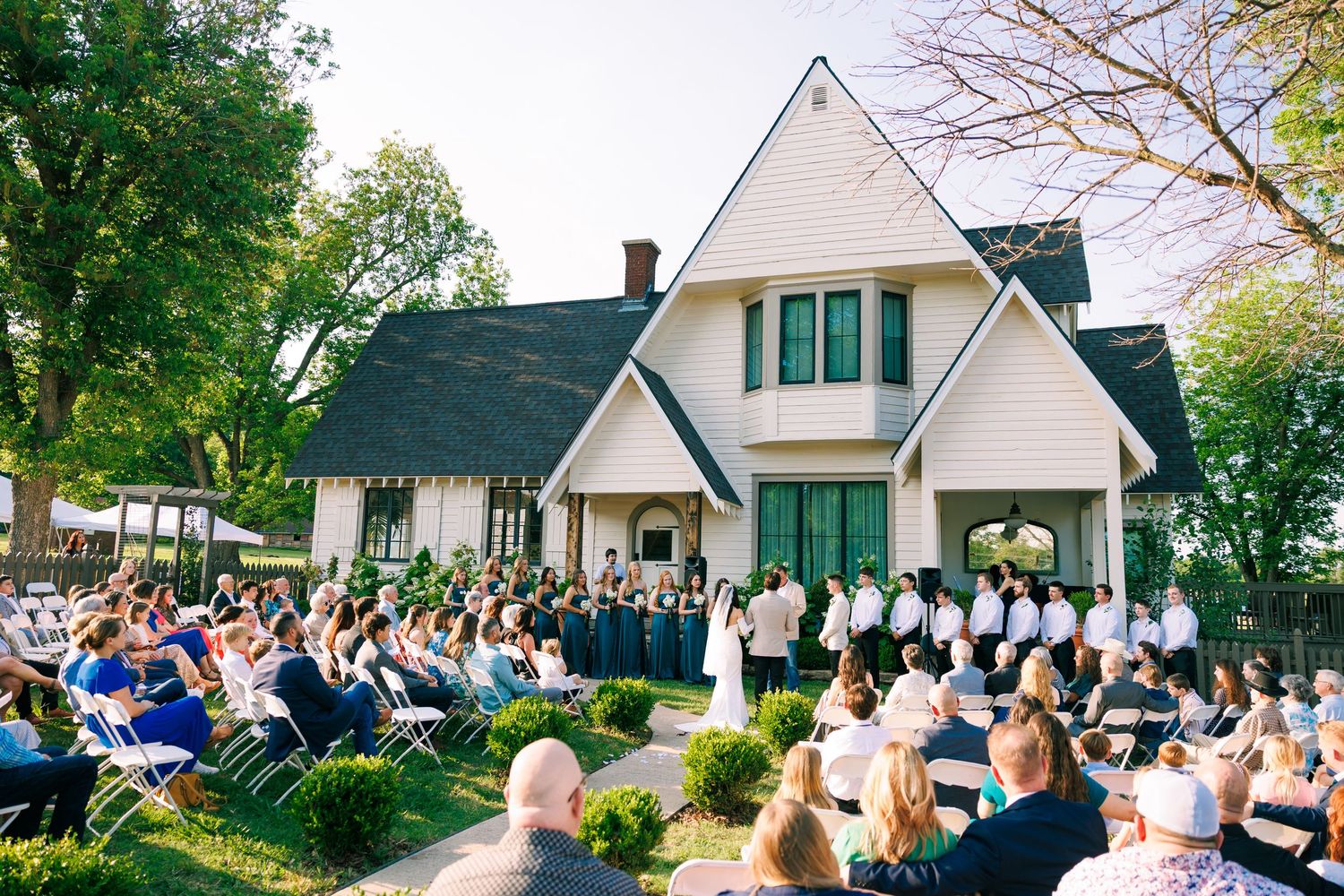 White country house wedding venue with guests gathered outside on a sunny day.