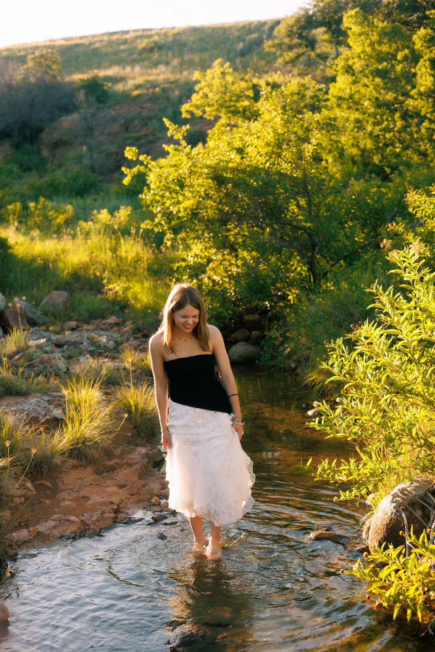 A person wading through a shallow stream at sunset surrounded by golden-lit vegetation.
