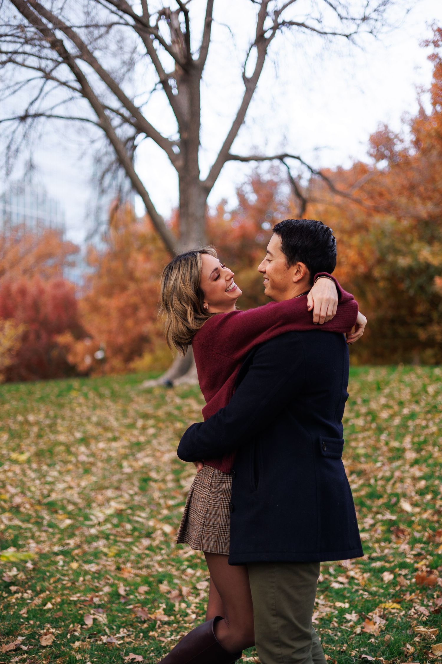 Playful autumn photoshoot in a park with fallen leaves and bare trees in the background.