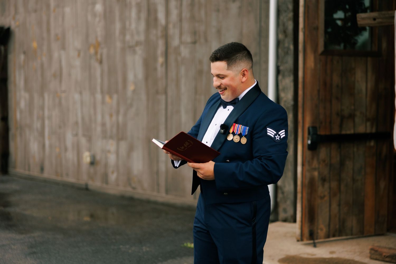 Military service member in dress blues reads from a book outside rustic wooden building.