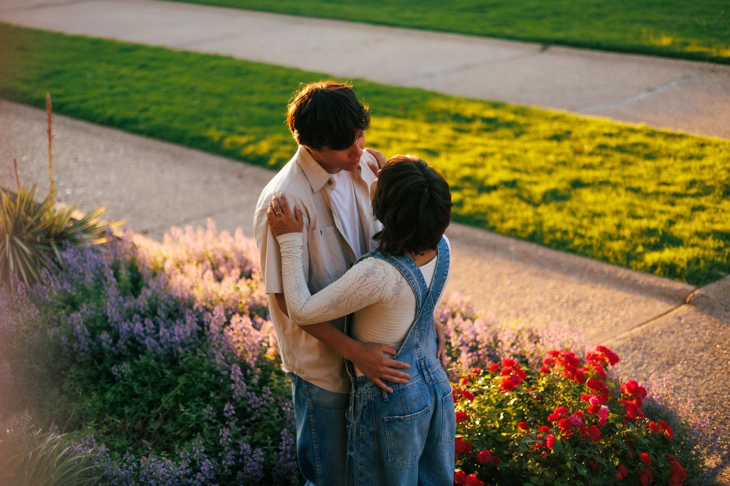 A couple strolls through a garden path lined with vibrant red flowers.