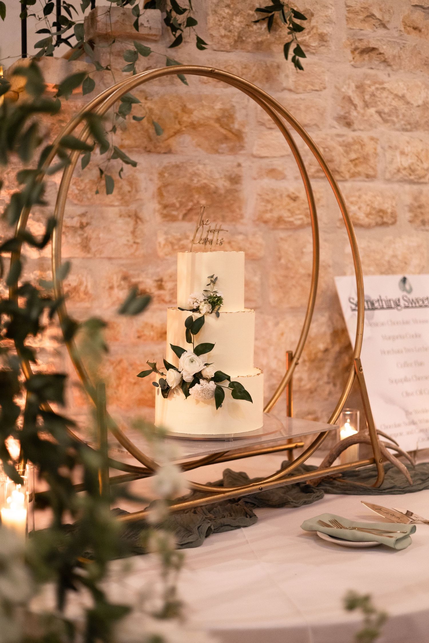 Elegant wedding table settings with gold hoops and greenery against a stone wall.