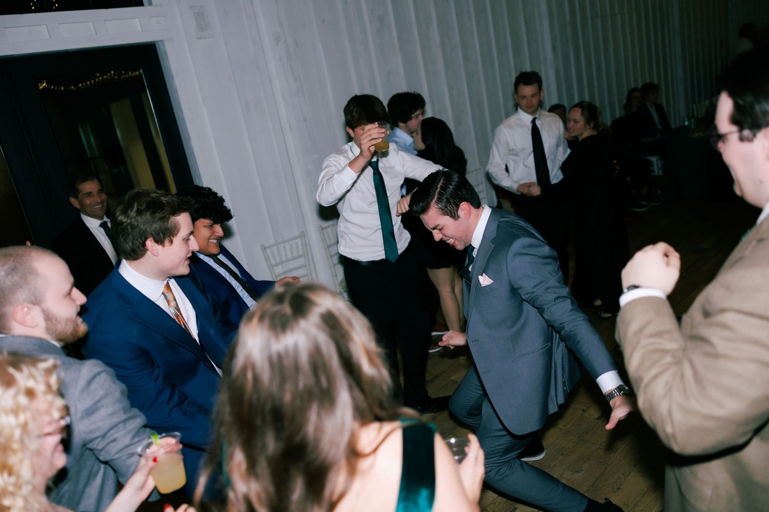 Wedding reception guests dancing and celebrating in dimly lit indoor venue.