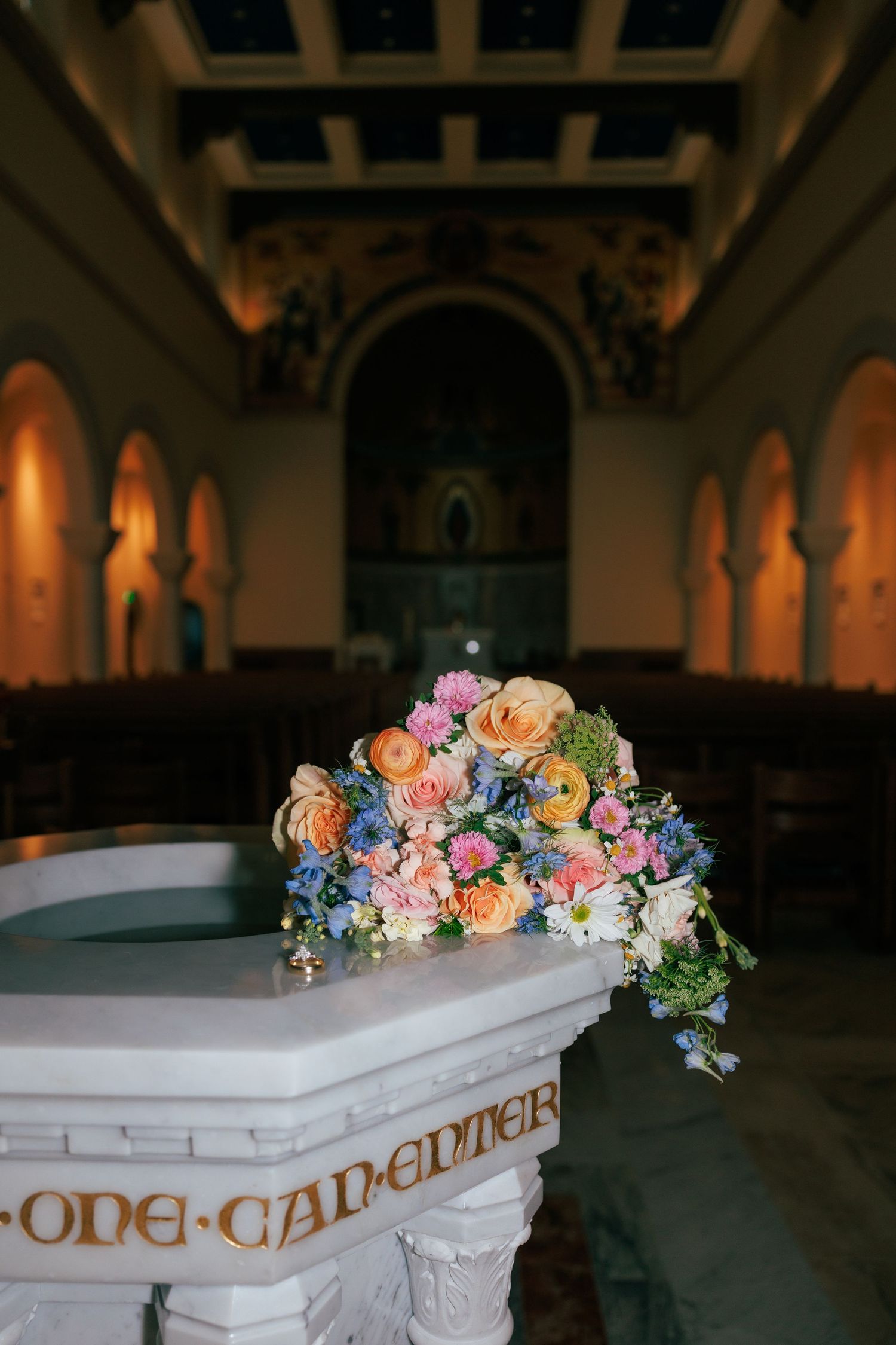 Decorative floral arrangements adorning white altar railings in a dimly lit church.